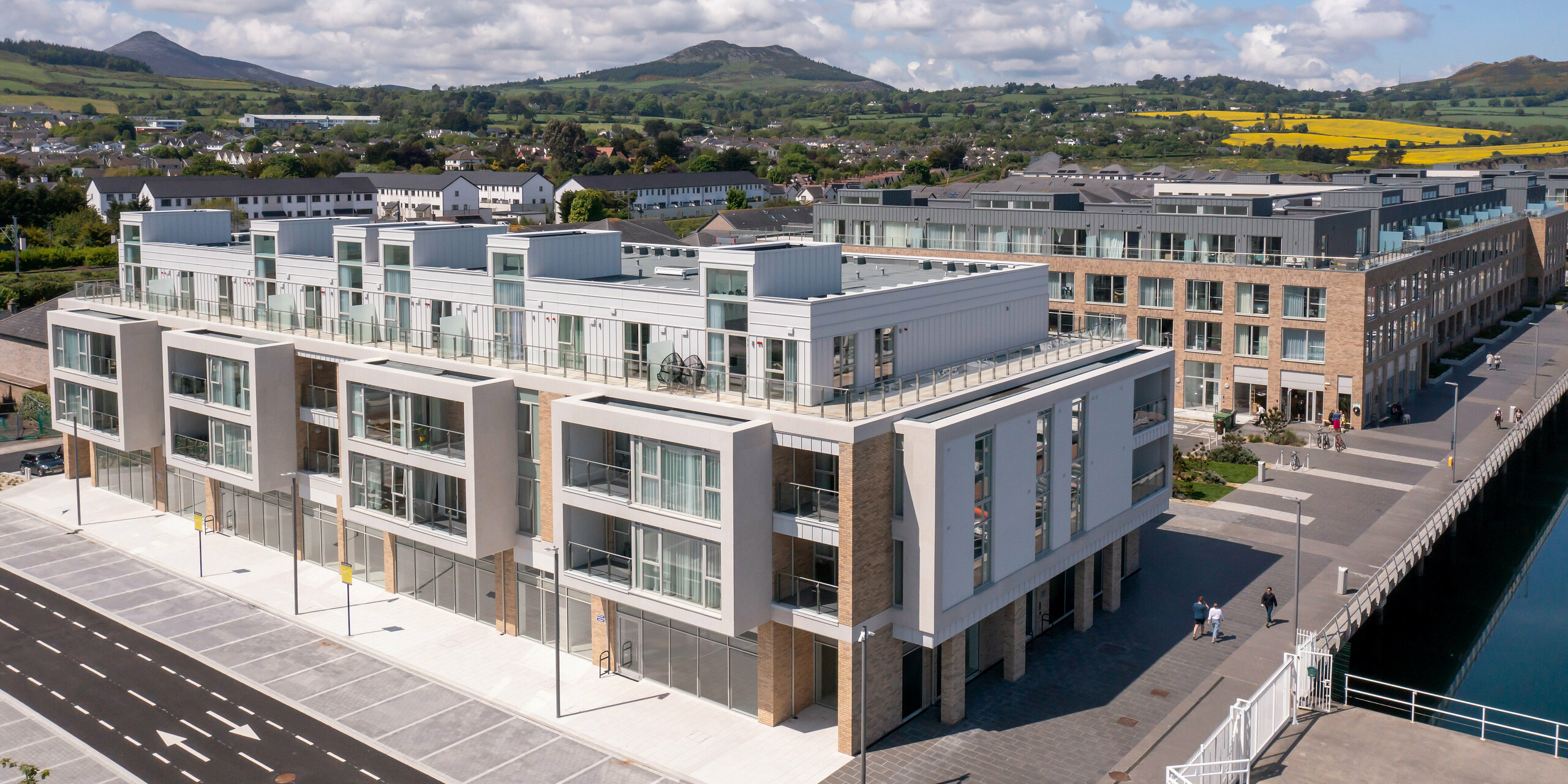 Marina Village Greystones in Wicklow, Irland – Weitwinkelaufnahme einer modernen Wohnsiedlung direkt am Wasser mit Blick auf den Yachthafen. Der Gebäudekomplex ist mit ca. 2.000 m² robustem PREFALZ in den Farben P.10 Prefaweiß und P.10 Hellgrau verkleidet. Die elegante Architektur umfasst große Glasfronten, geräumige Balkone und eine ästhetische Fassadengestaltung. Umgeben von einer malerischen Landschaft und hochwertigem Blech von PREFA bietet die Siedlung dauerhaften Schutz und zeitlose Ästhetik für exklusives Wohnen am Meer.