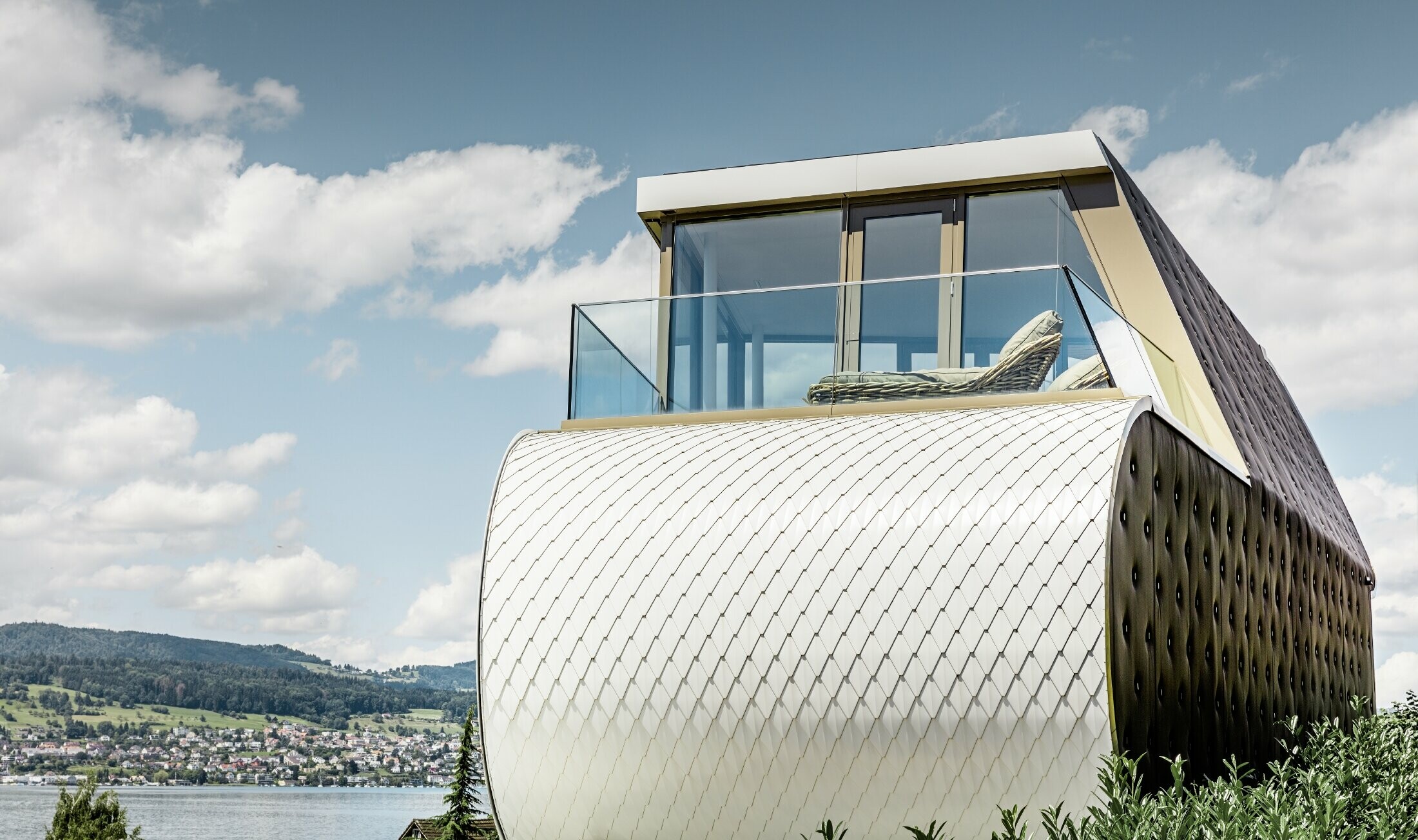 Bilde fra siden av det fremragende Flexhouse, designet av arkitekt Camenzind. Man kan se én av de buede ytterveggene kledd med PREFAs skjellete aluminiumsfasade i rent hvitt.