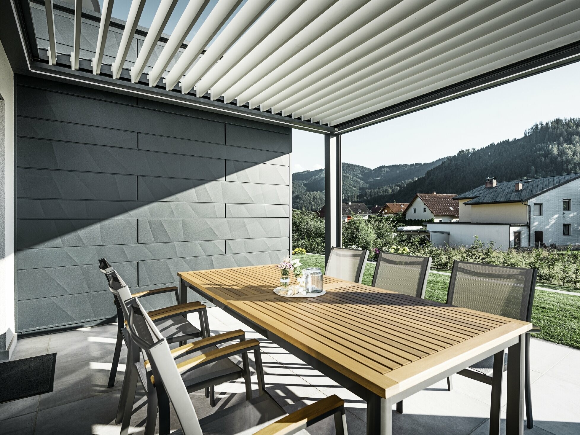 Overbygd og beskyttet terrasse med lameller, bord og stoler; én fasadeside er kledd med PREFA Siding.X fasadepaneler i antrasitt.
