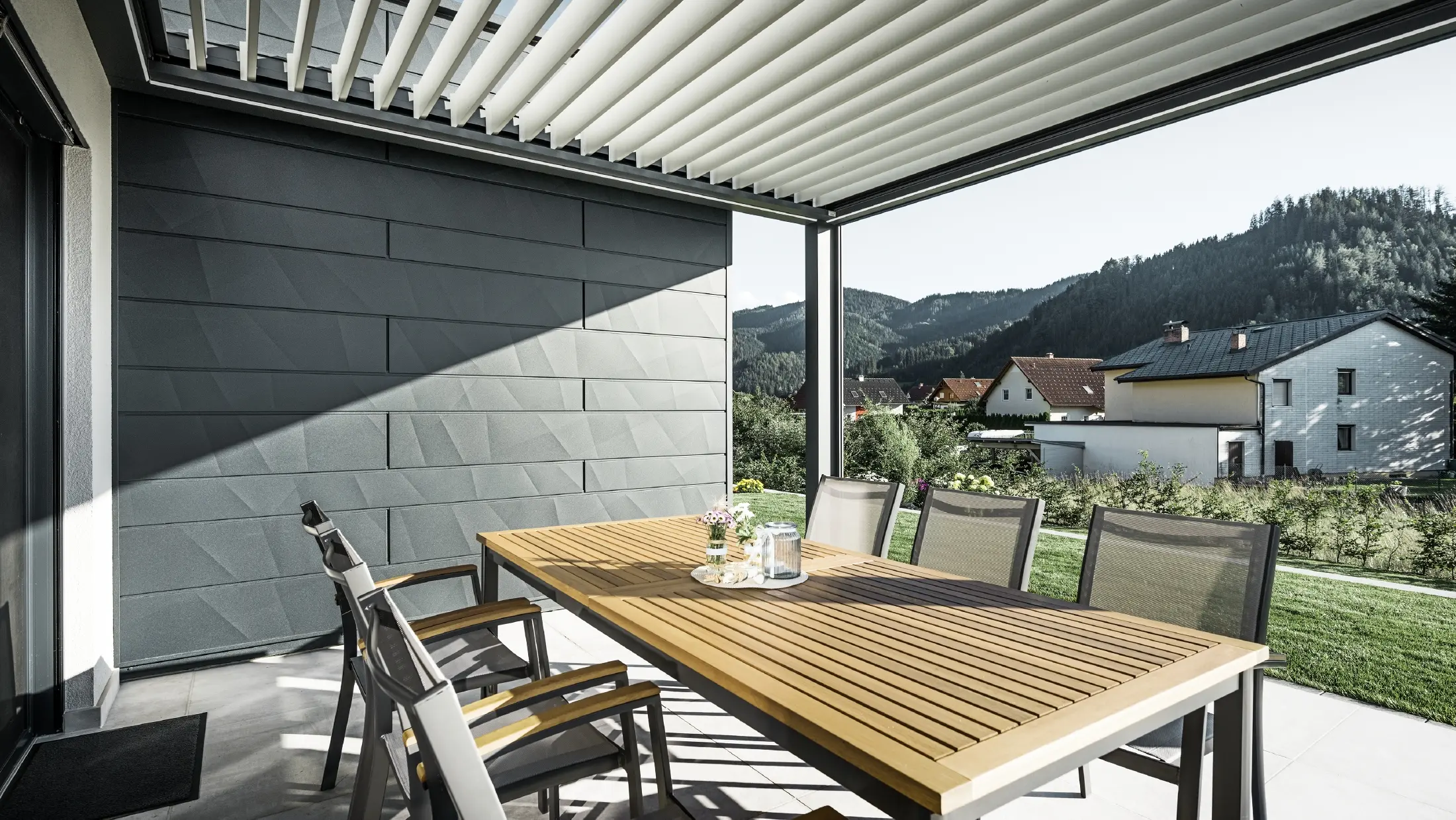 Overbygd og beskyttet terrasse med lameller, bord og stoler; én fasadeside er kledd med PREFA Siding.X fasadepaneler i antrasitt.