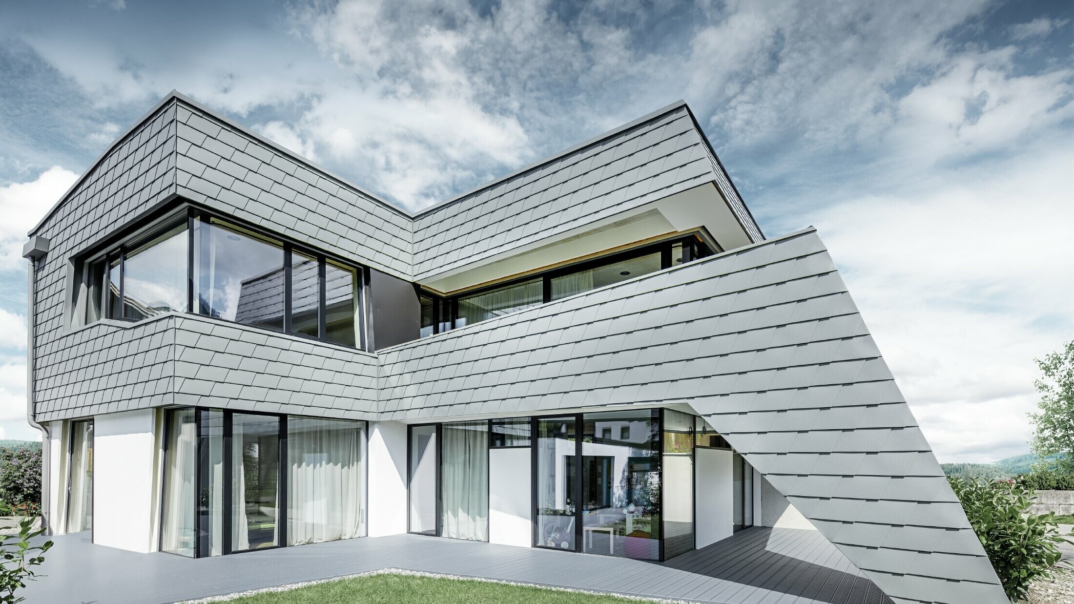 Moderne enebolig med flatt tak, store vindusflater og singelfasade i lys grå aluminium fra PREFA.