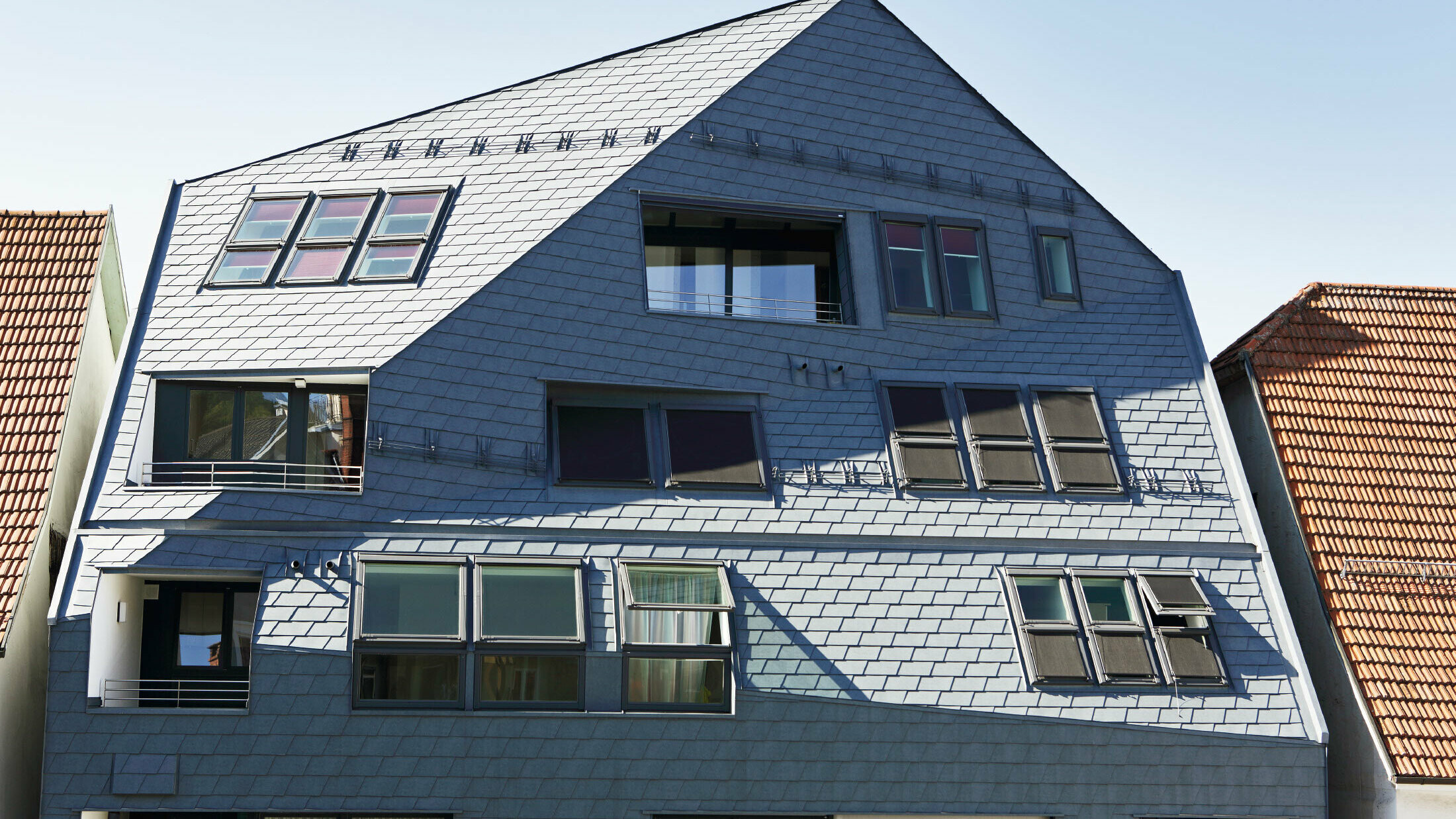 Kontorbygg med kantet fasadeflate, kledd med PREFA tak- og veggshingel i P.10 steingrå med mange vinduer