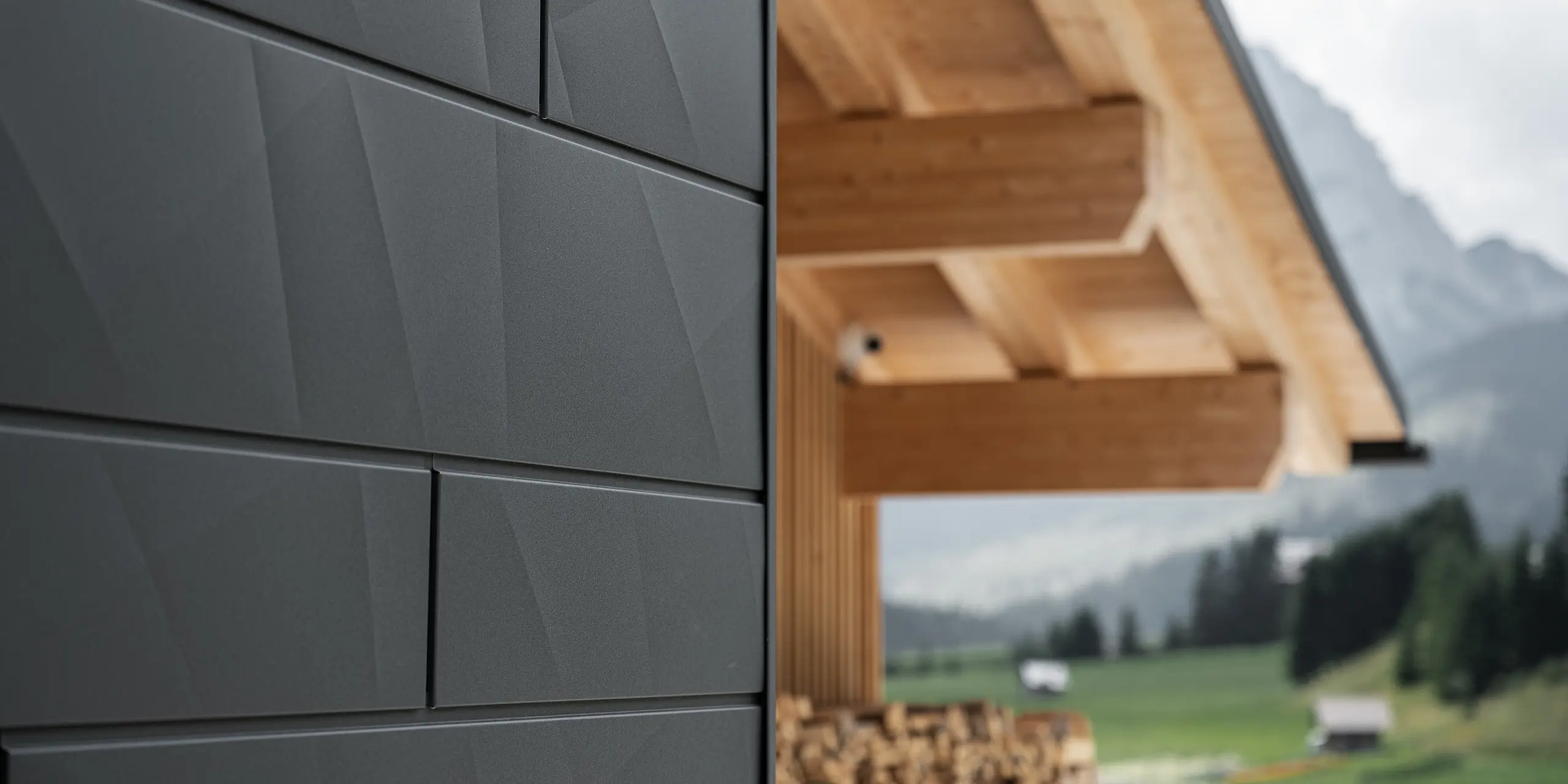 Nærbilde av Siding.X fasadepaneler i P.10 svart fra PREFA på Casa Hoffe i Sappada, Italia. Fasadesystemet i aluminium er montert i et moderne, abstrakt design som skaper en vakker kontrast til de synlige treelementene i takkonstruksjonen. Den innovative fasadeløsningen glir sømløst inn i det alpine miljøet og representerer en kombinasjon av funksjonalitet, holdbarhet og estetisk byggeskikk.