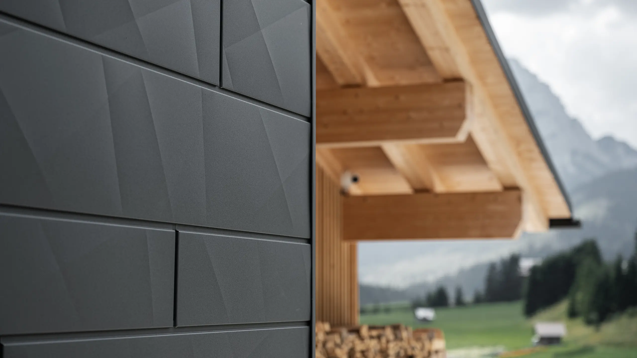 Nærbilde av Siding.X fasadepaneler i P.10 svart fra PREFA på Casa Hoffe i Sappada, Italia. Fasadesystemet i aluminium er montert i et moderne, abstrakt design som skaper en vakker kontrast til de synlige treelementene i takkonstruksjonen. Den innovative fasadeløsningen glir sømløst inn i det alpine miljøet og representerer en kombinasjon av funksjonalitet, holdbarhet og estetisk byggeskikk.