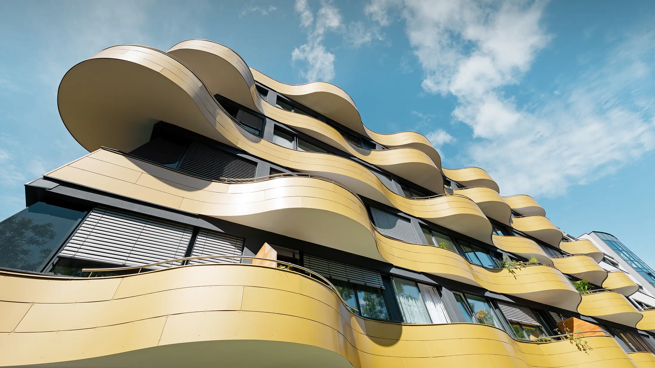Froschperspektive auf die einzigartige Fassadengestaltung der Wohnhausanlage "Goldene Welle" in Graz. Die goldenen Balkone mit ihren speziellen Rundungen wurden mit Aluminium Verbundplatten bekleidet.