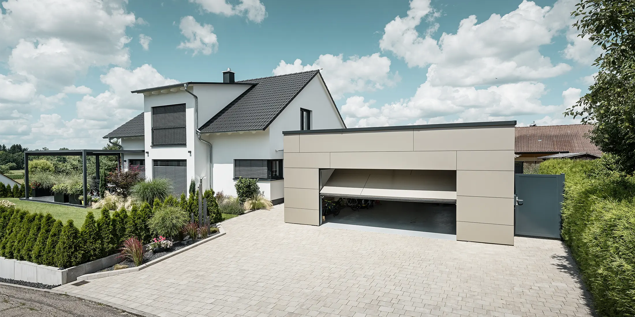 Die Fassade der Garage des Einfamilienhauses wurde komplett mit der PREFABOND Aluminium Verbundplatte in Bronze verkleidet. Das Garagentor ist geöffnet, davor ist eine große Einfahrt für mindestens 2 Autos gepflastert. 