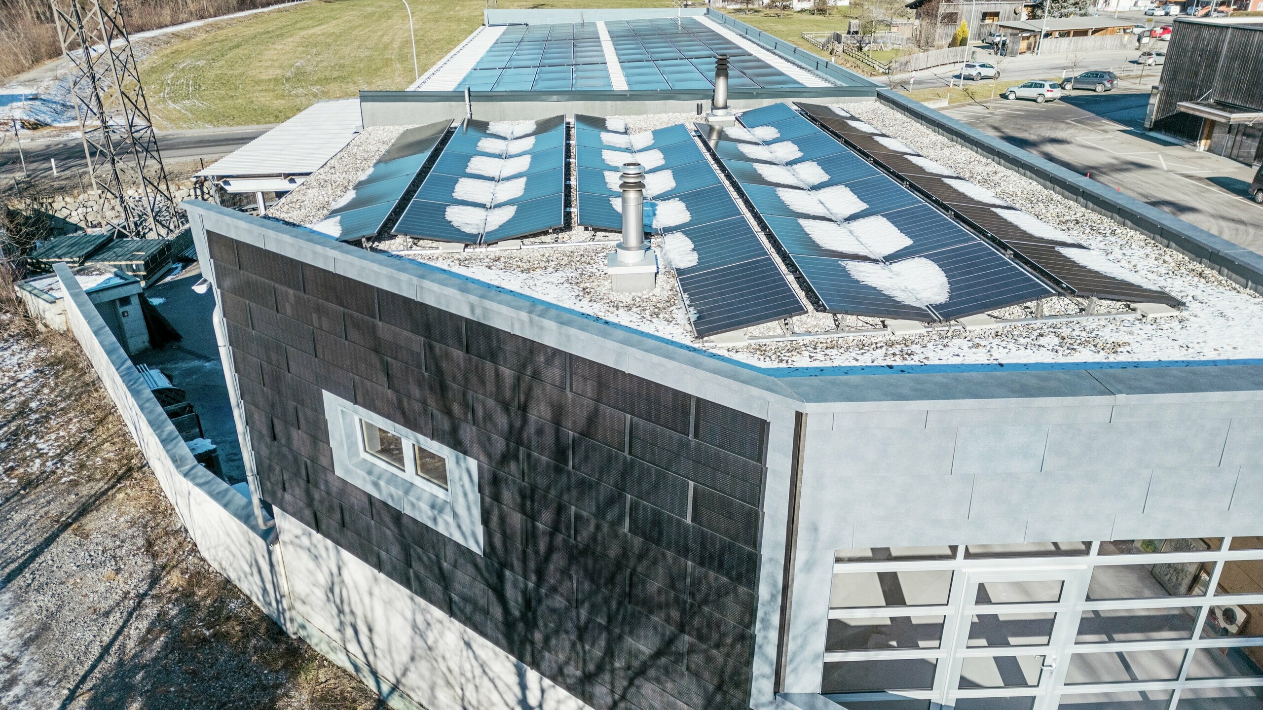  Das Bild zeigt eine Vogelperspektive des RÜMA-Bürogebäudes in Vorarlberg. Die Fassade ist mit PREFA-Solardachpaneelen zur nachhaltigen Stromerzeugung ausgestattet.