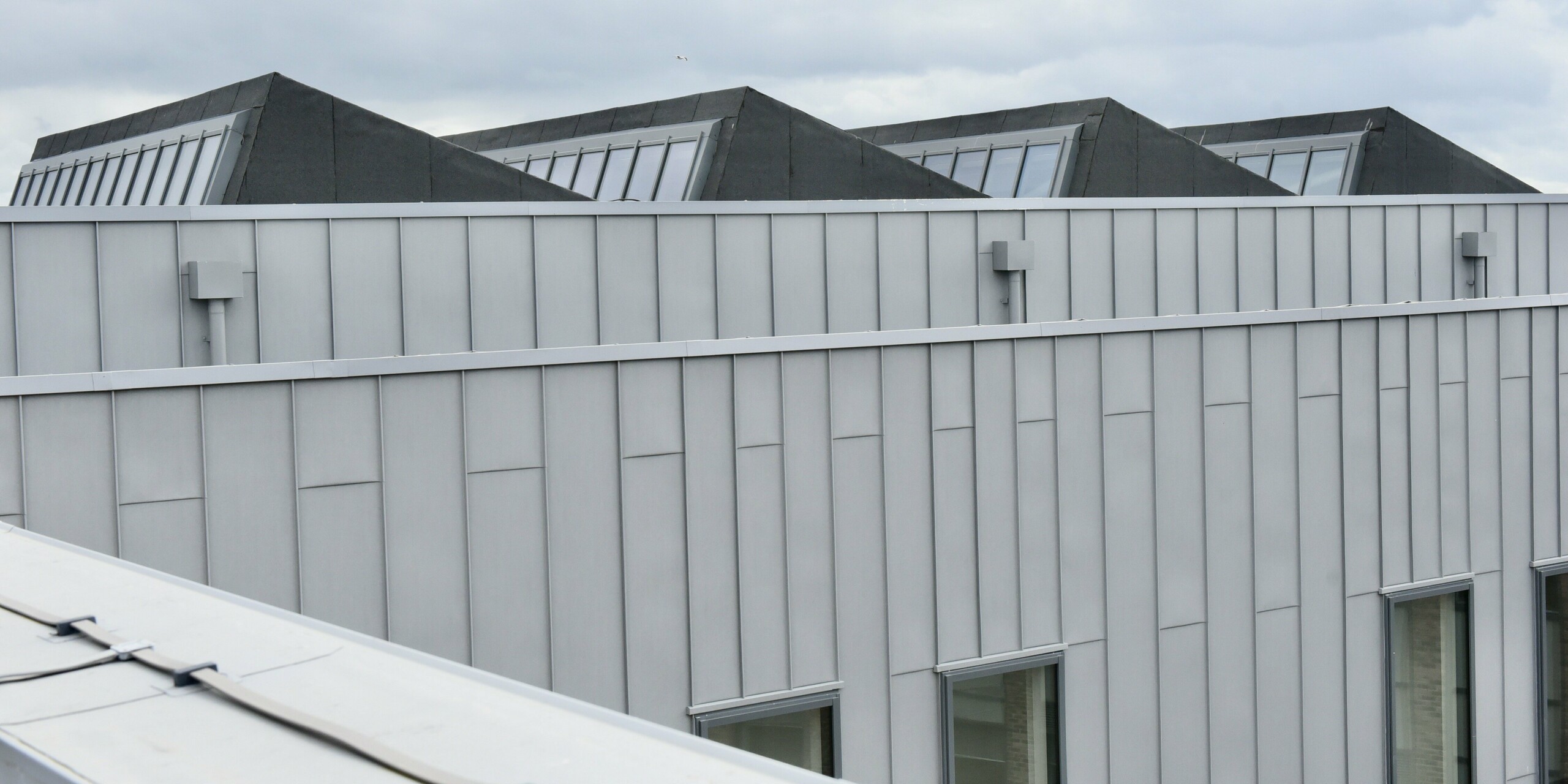 Nahaufnahme des Dachgeschosses des North Regional College. Die patinagraue PREFALZ-Fassade zeigt die Qualität der Aluminiumverkleidung und unterstreicht das durchdachte Design des Gebäudes. 