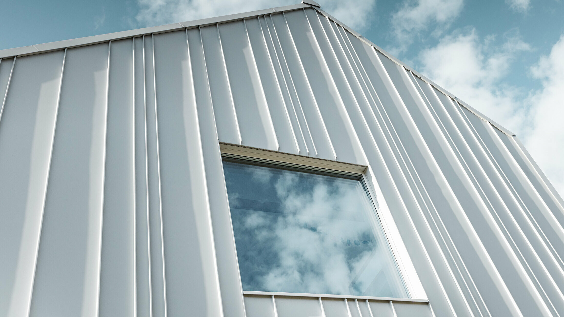 hvit PREFALZ som vinklet stående fals på fasade med forskjellige panelbredder og et vindu