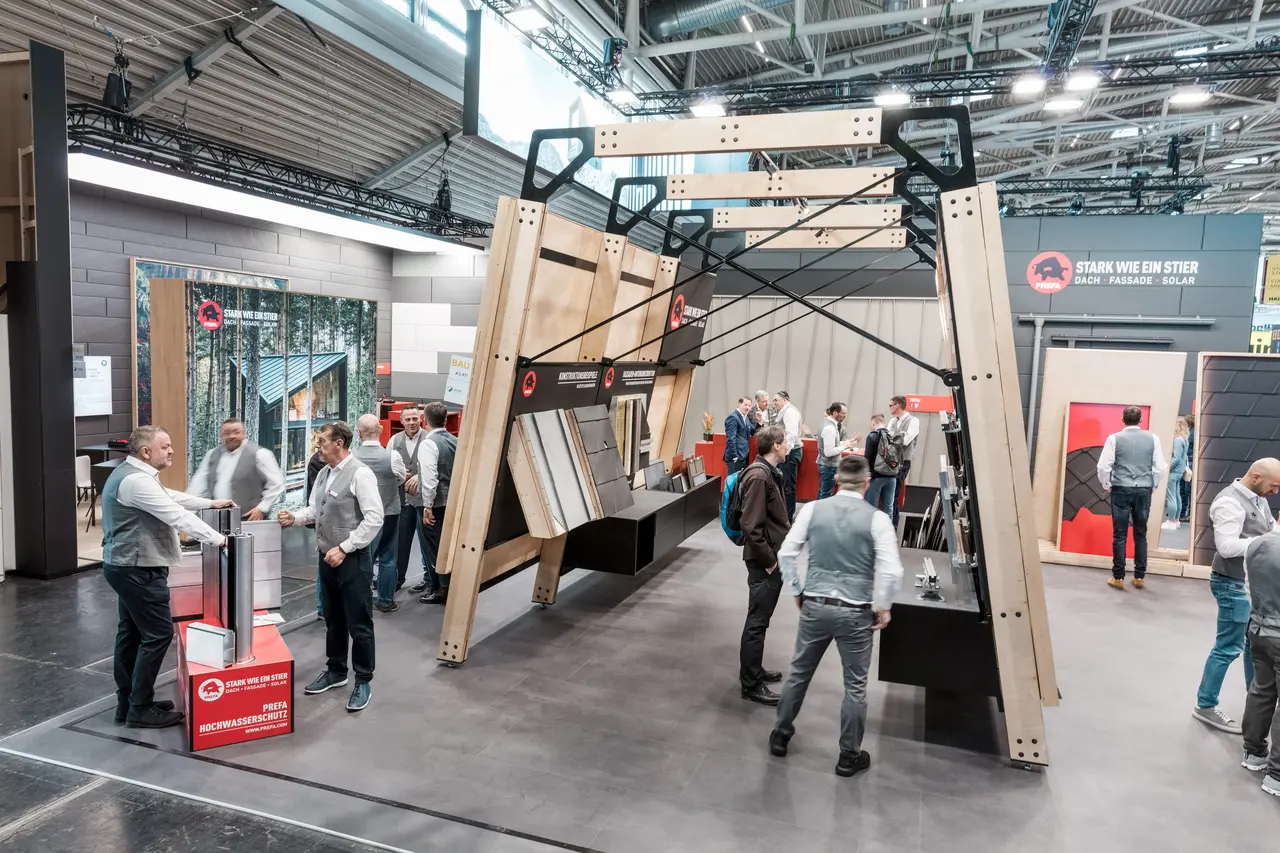Den livlige PREFA-messestanden med messevegger som viser PREFAs tak- og fasadeprodukter i aluminium.
