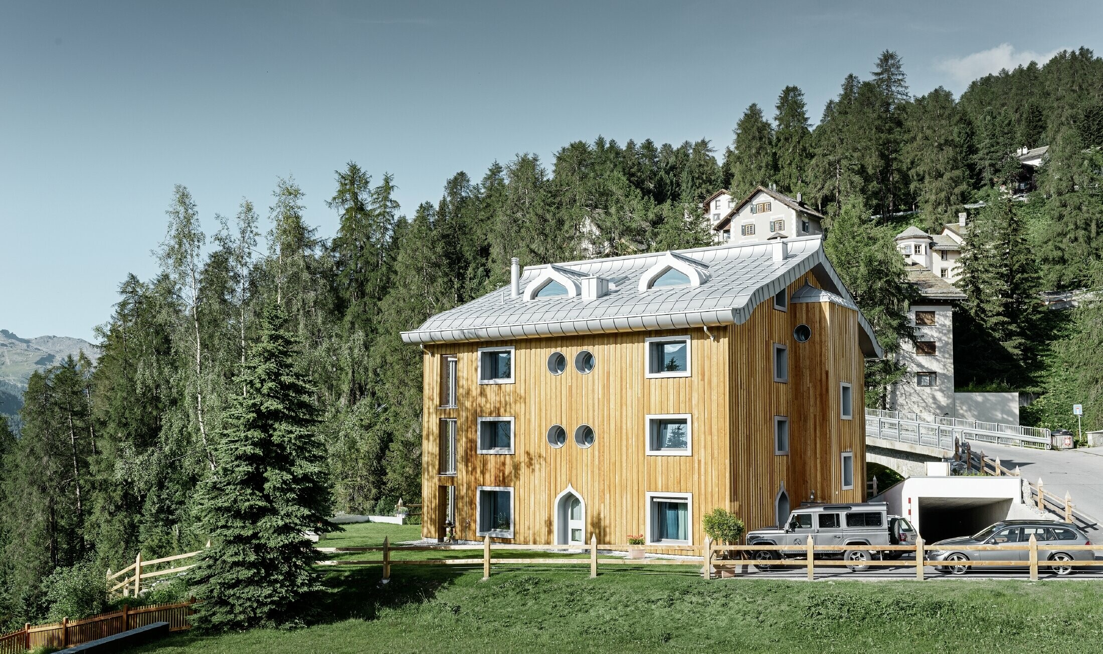 Wohnhausanlage in St. Moritz mit Holzfassade und Aluminiumdach mit geschwungener Traufe in silbermetallic