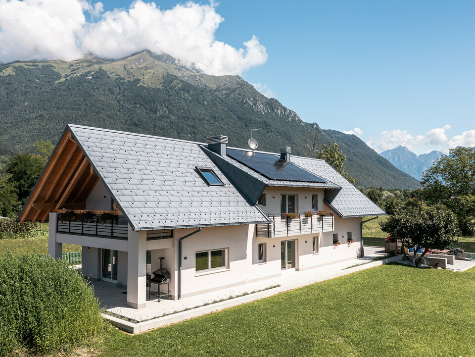 Drohnenaufnahme eines Hauses in Belluno, Italien, eingedeckt mit PREFA R.16 Dachplatten in P.10 anthrazit. Das Anwesen liegt in einer atemberaubenden Alpenlandschaft und kombiniert traditionelle Elemente wie freiliegende Holzgiebel mit modernen, langlebigen Baumaterialien, wodurch eine perfekte Symbiose aus Tradition und Moderne entsteht.