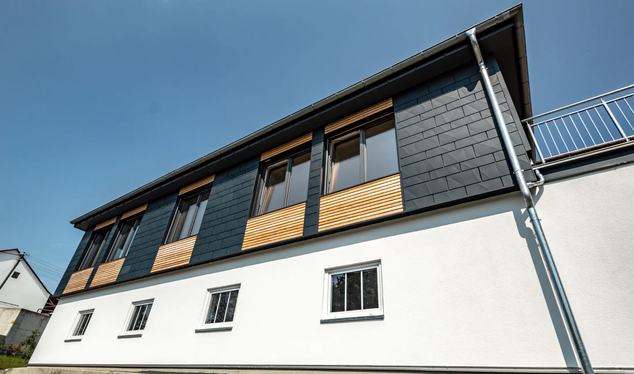 Fasadeutforming med forskjellige materialer: Det som er brukt, er aluminium PREFA Siding.X i antrasitt, en horisontal trefasade og en hvit gipsfasade.