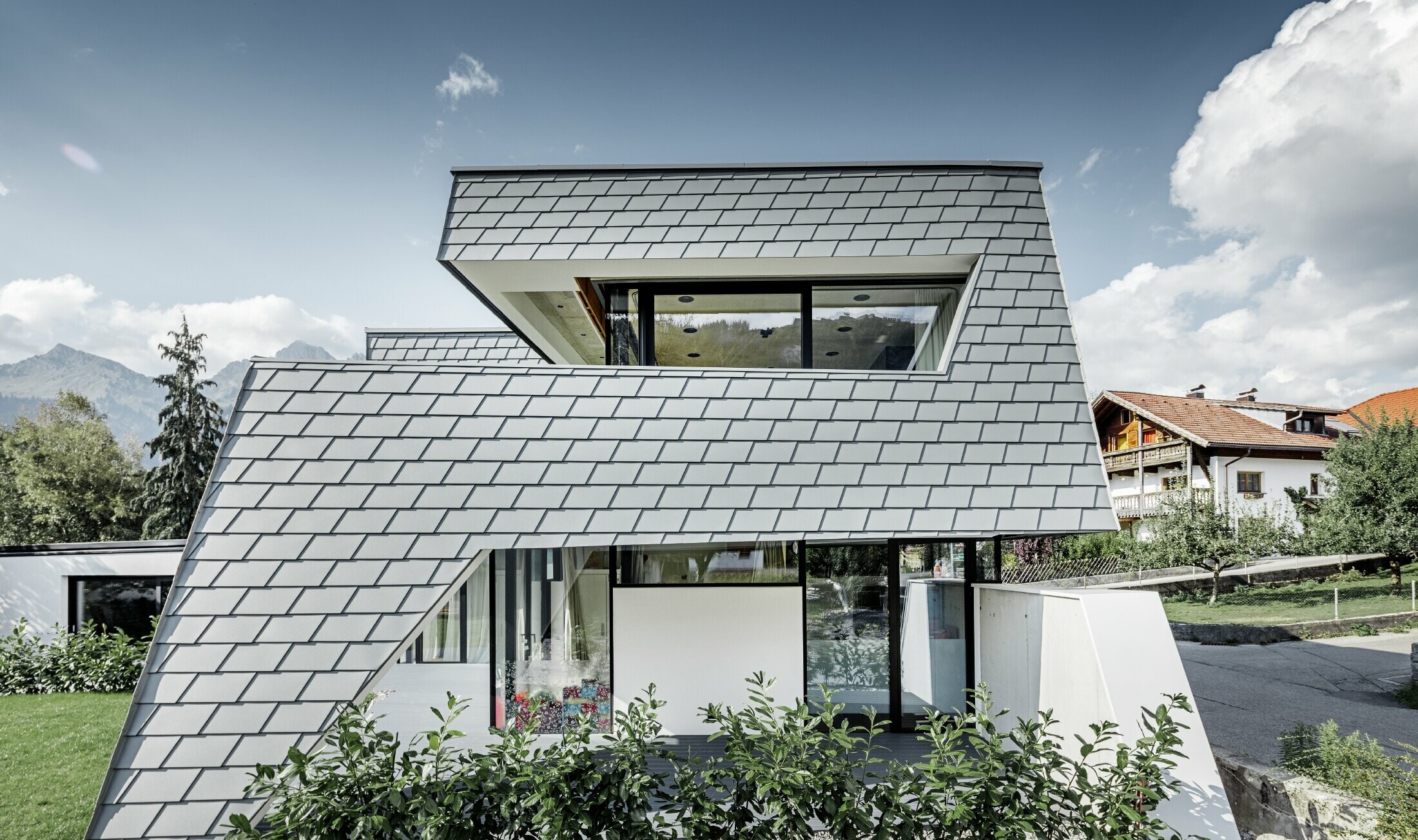modernes Einfamilienhaus mit Flachdach, großen Fensterflächen und einer Schindel-Fassade in hellgrau aus Aluminium von PREFA