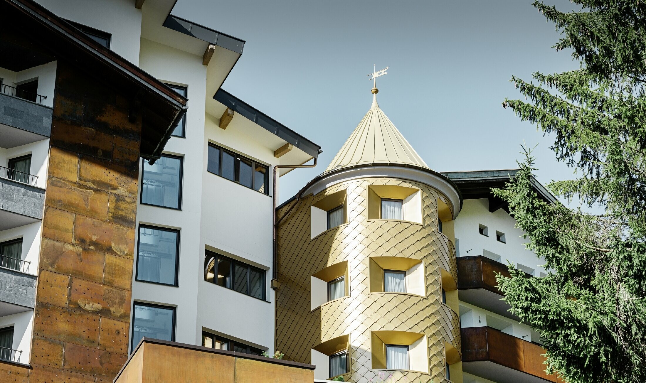 traditionelles Hotel in Ischgl mit Holzbalkonen und Holzfassade und einem Turm mit goldenen Alu-Rauten von PREFA