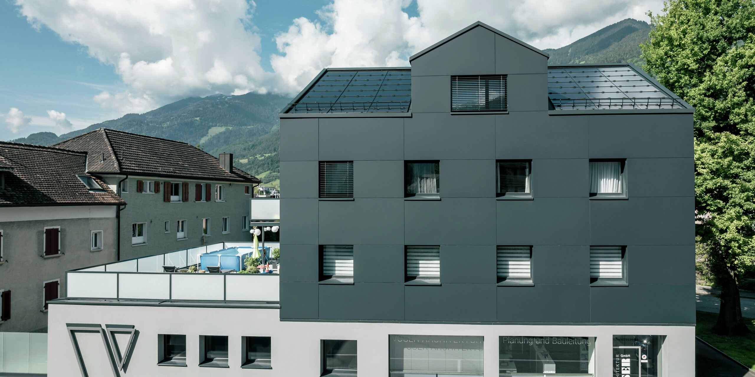 Frontalansicht eines sanierten Geschäftsgebäudes nach der Fassadensanierung mit PREFABOND Aluminium-Verbundplatten in Anthrazit. Die klare und hochwertige Fassade verleiht dem Gebäude eine elegante und zeitgemäße Optik. Im Erdgeschoss befinden sich große Fensterflächen, die das Architekturbüro Voser repräsentieren.