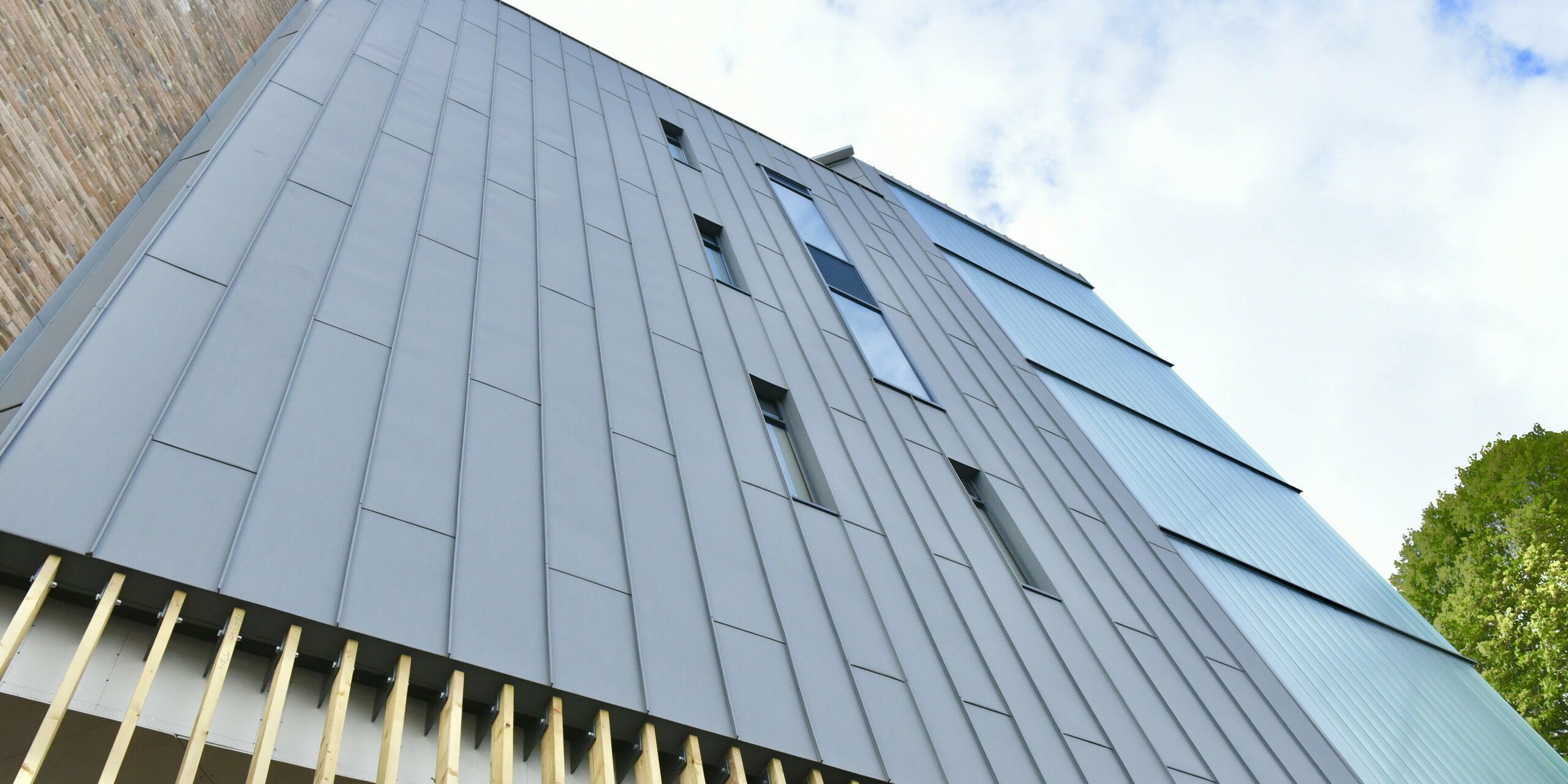 Detailansicht der PREFALZ Stehfalzverkleidung in Patinagrau am North Regional College. Die präzise Verarbeitung des Aluminiums unterstreicht den nachhaltigen und modernen Charakter der Fassade, die sich harmonisch in die Gesamtarchitektur einfügt.
