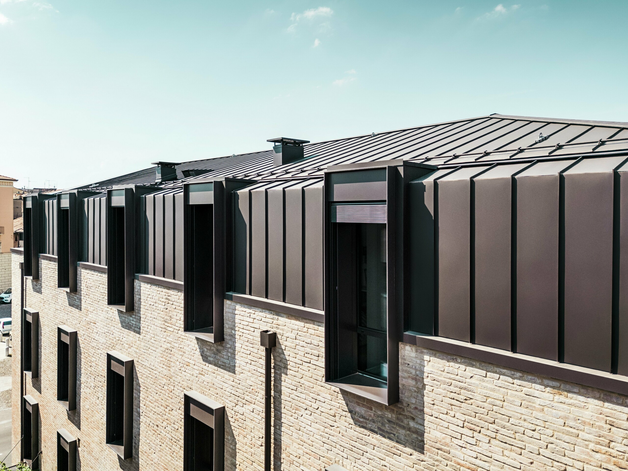 Modernes Dach- und Fassadendesign eines Backsteinhauses in Italien mit PREFALZ Aluminiumdach in P.10 Haselnussbraun und markanten Oberlichtern (Giebeln).