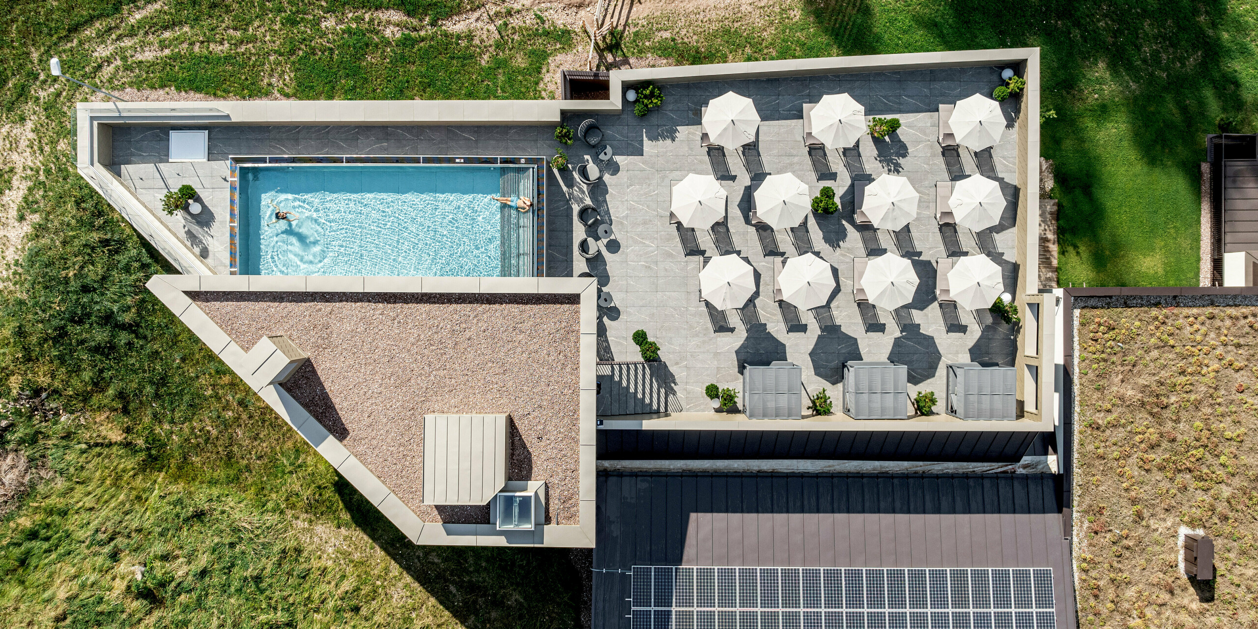 Die Draufsicht zeigt das moderne Sporthotel Obereggen in Südtirol mit seiner großzügigen Sonnenterrasse und dem Outdoor-Pool. Die PREFA Aluminiumfassade und Attika in Bronze setzen einen markanten visuellen Akzent und heben sich wirkungsvoll von der grünen alpinen Landschaft ab. Die langlebigen, witterungsbeständigen und wartungsarmen PREFA Aluminiumprodukte überzeugen durch ihre elegante Optik, hohe Stabilität und nachhaltige Qualität – ideal für anspruchsvolle Architektur im alpinen Raum.