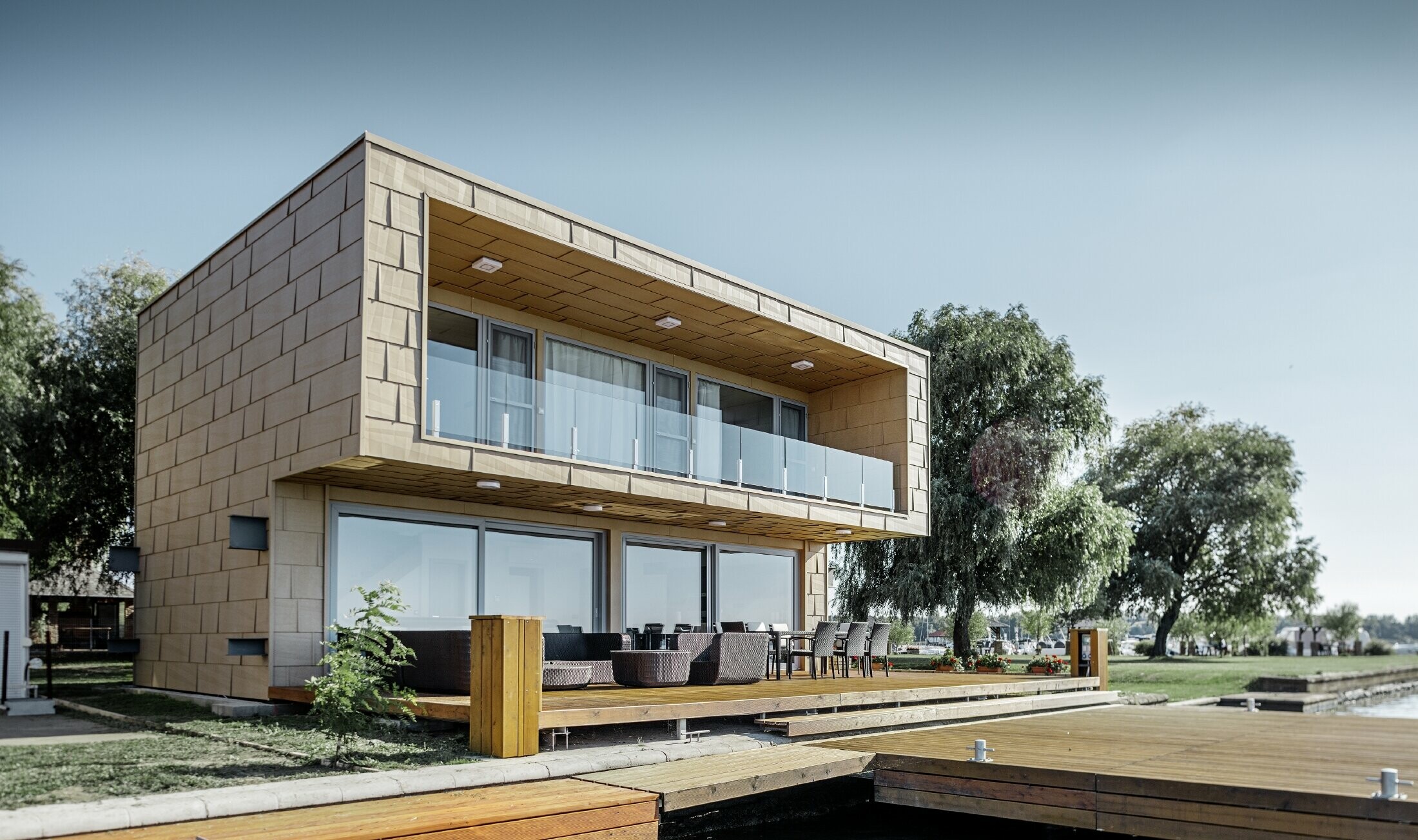 modernes Wochenendhaus mit Flachdach und großen Fensterflächen am See mit einer gekanteten Aluminiumfassade in sandbraun