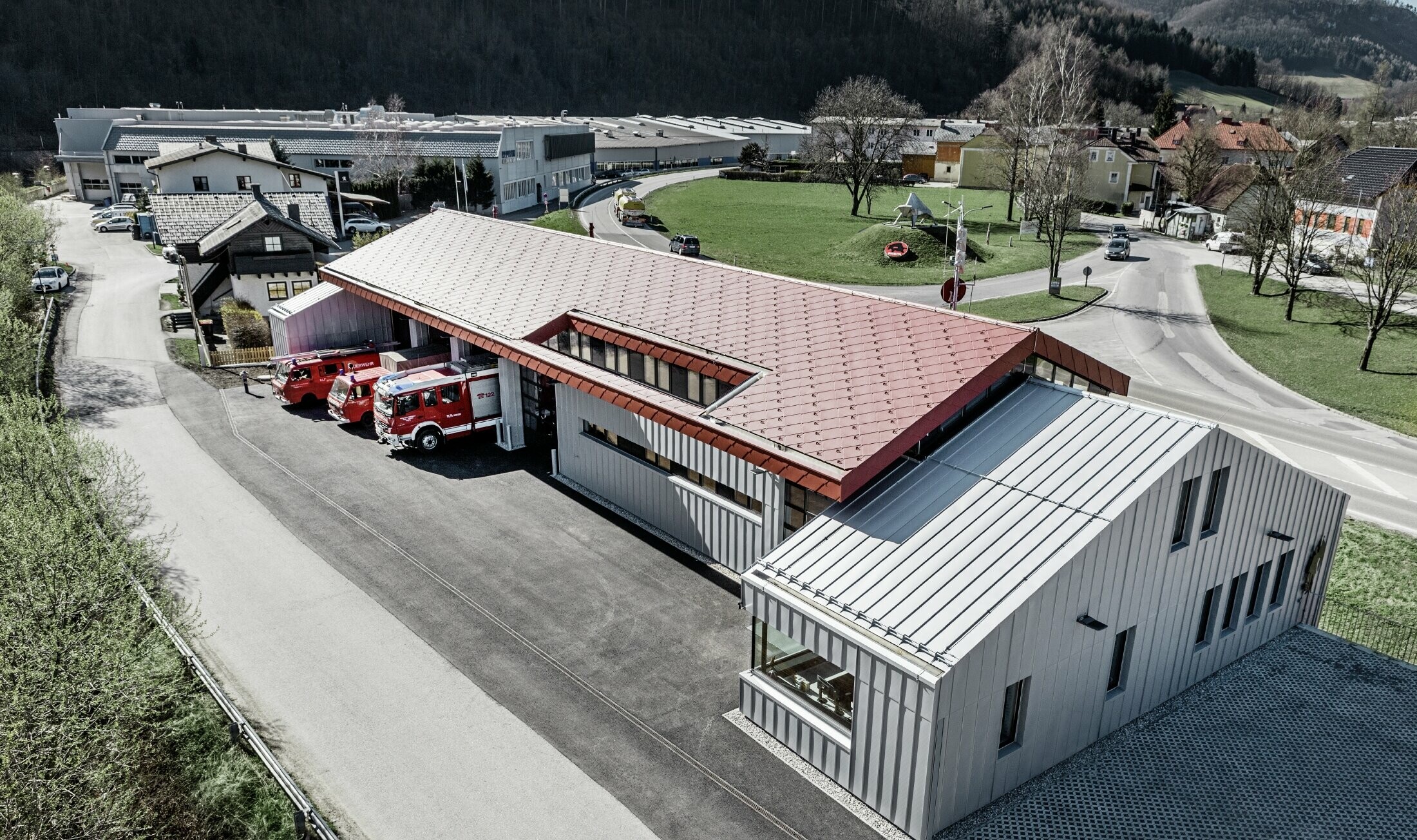 Foto av brannstasjonen i Marktl/Lilienfeld i fugleperspektiv. Den venstre bygningsdelen er helt kledd med rombe 44 i oksydrød på tak og fasade. Den høyre delen blir et aluminiumsskall med Prefalz i sølvmetallic.