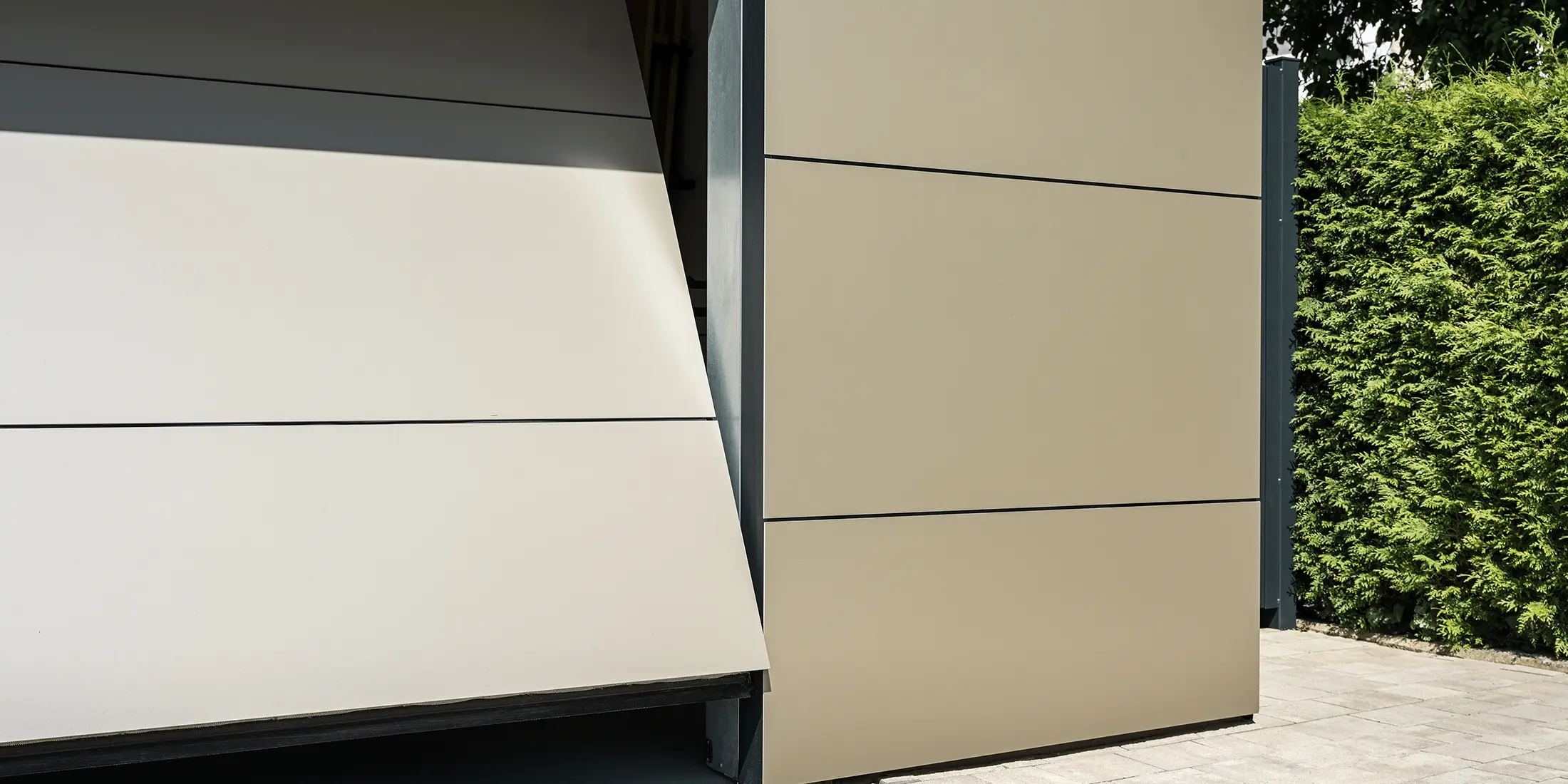 Nahaufnahme eines automatischen Garagentors. Die Garage und das automatische Garagentor sind mit bronzefarbenen Aluminium Verbundplatten verkleidet. Die präzise Verarbeitung spiegelt die Qualität der langlebigen Verbundplatten wider. Der schmale Öffnungsspalt gewährt einen kleinen Einblick in das Innere der Garage.