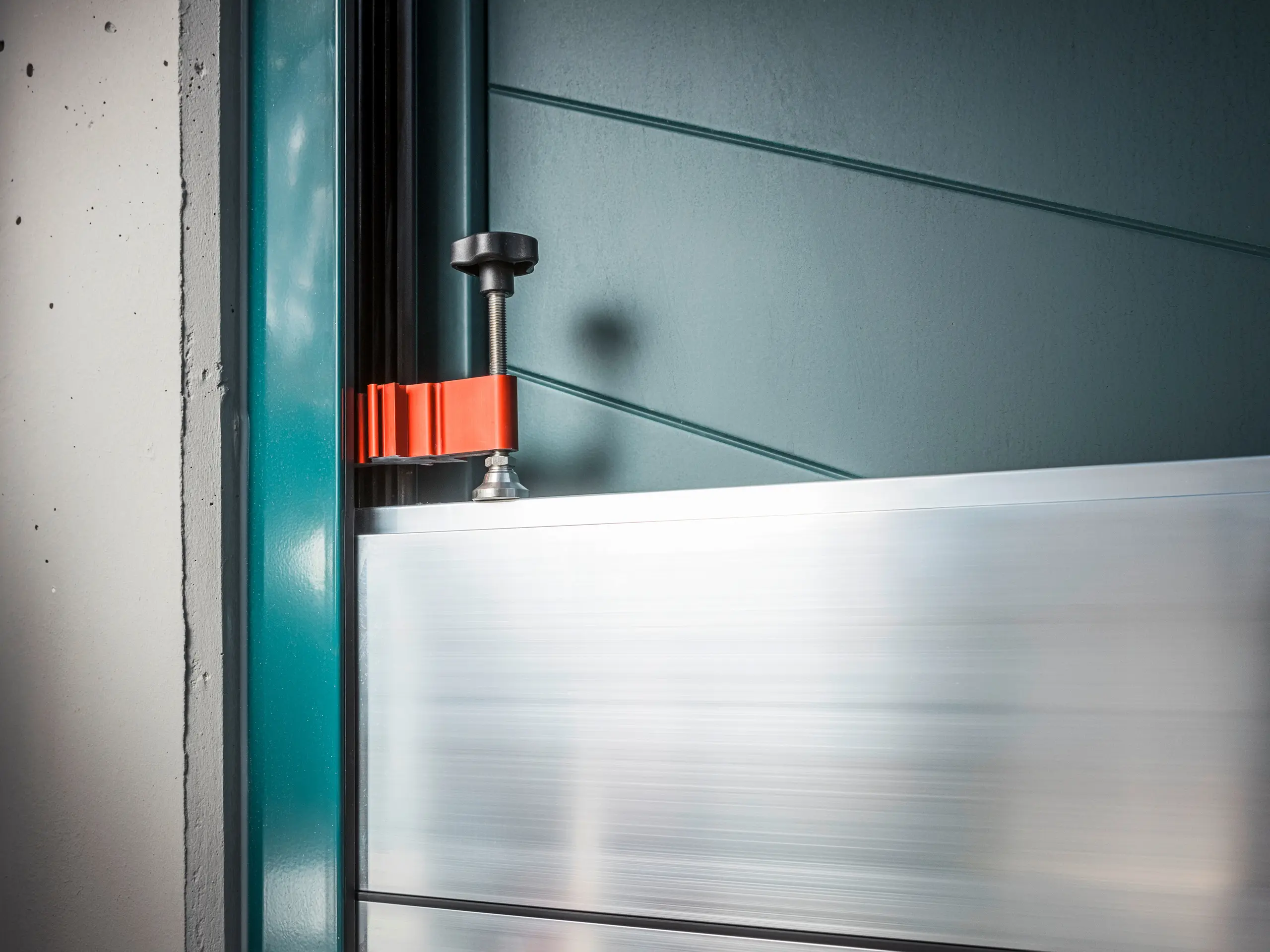 Nærbilde av PREFAs flomsikringssystem på en portramme, som består av dambjelker i aluminium festet med en robust, rød klemme (klemmestykket) for å gi sikker beskyttelse mot oversvømmelse.