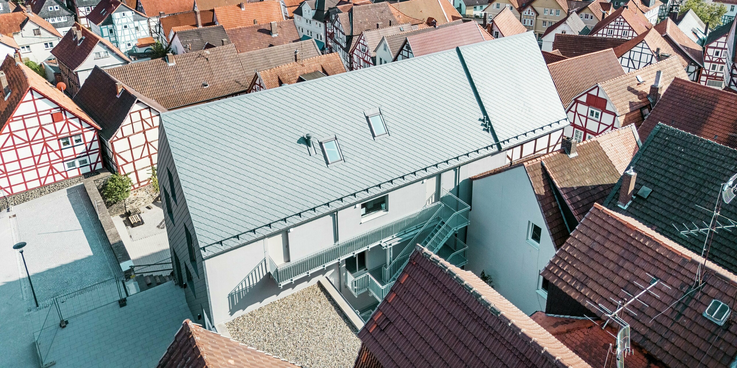 Weitwinkel-Drohnenansicht des Volkshauses in Homberg, DE, mit PREFA Dachrauten 29 × 29 in P.10 Steingrau. Das moderne Dachdesign aus robustem Aluminium fügt sich harmonisch in die historische Altstadt mit ihren roten Ziegeldächern ein und bietet Langlebigkeit, Witterungsschutz und zeitlose Eleganz.