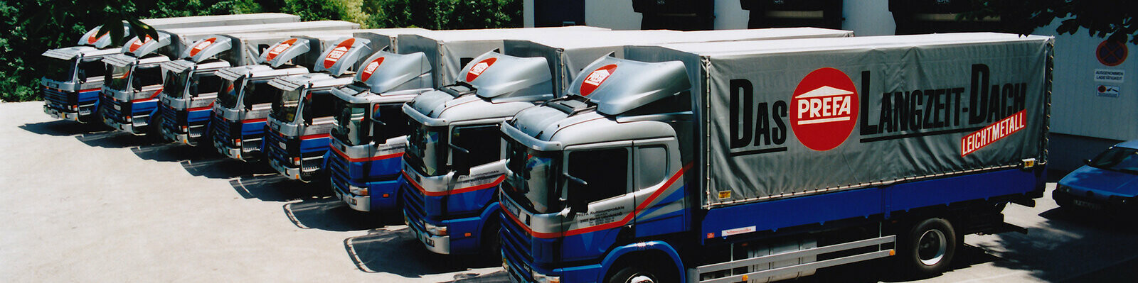Åtte eldre PREFA-lastebiler i blått og sølv med PREFA-logo på rad og rekke 