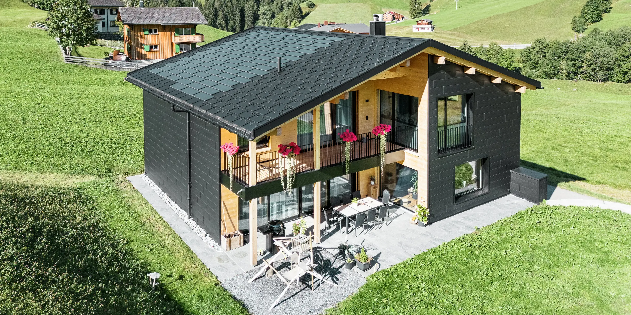Den elegante eneboligen i de kuperte omgivelsene i Ascharina (Sveits) viser hvordan aluminium og tre kan kombineres perfekt. De robuste PREFA Siding.X-fasadepanelene i P.10 svart harmonerer med taket som består av PREFA soltakpaneler og R.16 takpaneler i samme farge. Den slitesterke aluminiumskledningen beskytter bygningen mot utfordringene i det alpine klimaet på en pålitelig måte.