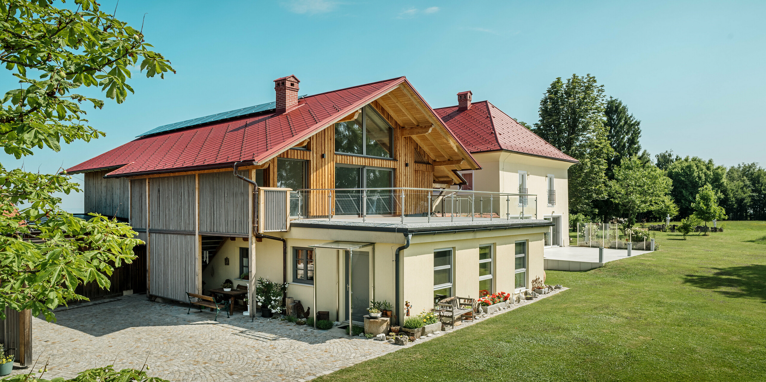 Die beiden sanierten Einfamilienhäuser in Aschach an der Steyr beeindrucken durch ihre harmonische Dachgestaltung. Die PREFA Dachraute 44 x 44 in der Farbe P.10 Oxydrot verleiht ihnen ein markantes, zeitloses Aussehen und bildet einen starken Kontrast zur modernen Holzverkleidung bzw. der gelblichen Putzfassade. Hervorzuheben sind zudem die großflächigen Fenster, welche die Offenheit des Obergeschosses noch verstärken. Das großzügige Grundstück und die gepflegte Gartenlandschaft betonen die gelungene Verbindung von Natur, Tradition und Moderne. Die PREFA Dachrauten sind nicht nur ästhetisch ansprechend, sondern auch äußerst beständig und langlebig – ideal für jedes Wetter.
