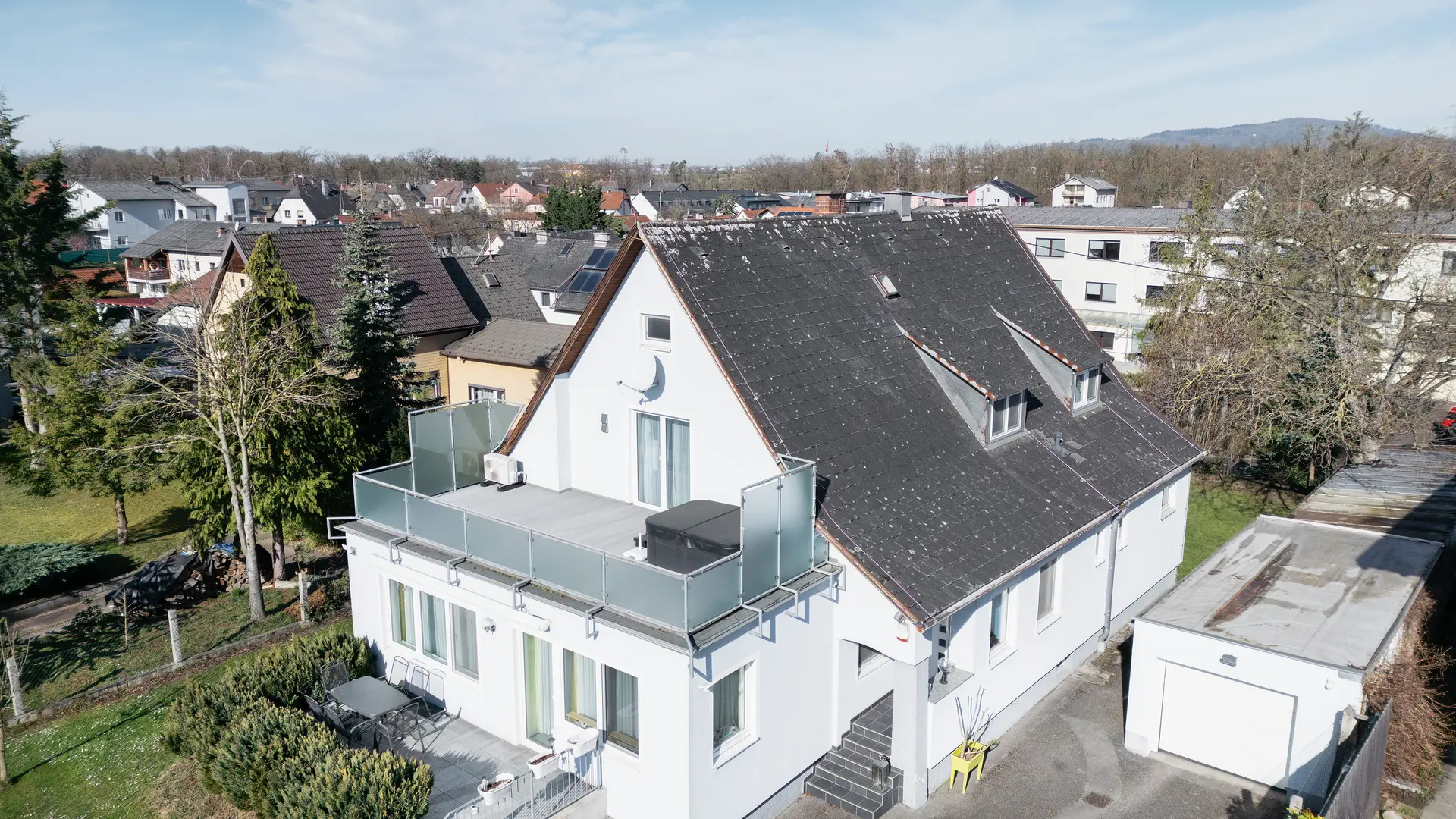 Fugleperspektiv på en bygning med et gammelt eternittak som er dekket av smuss og lav. Det er ingen solcelleanlegg å se på taket. Balkongen i forgrunnen har glassrekkverk og ligger i bygningens øverste etasje.