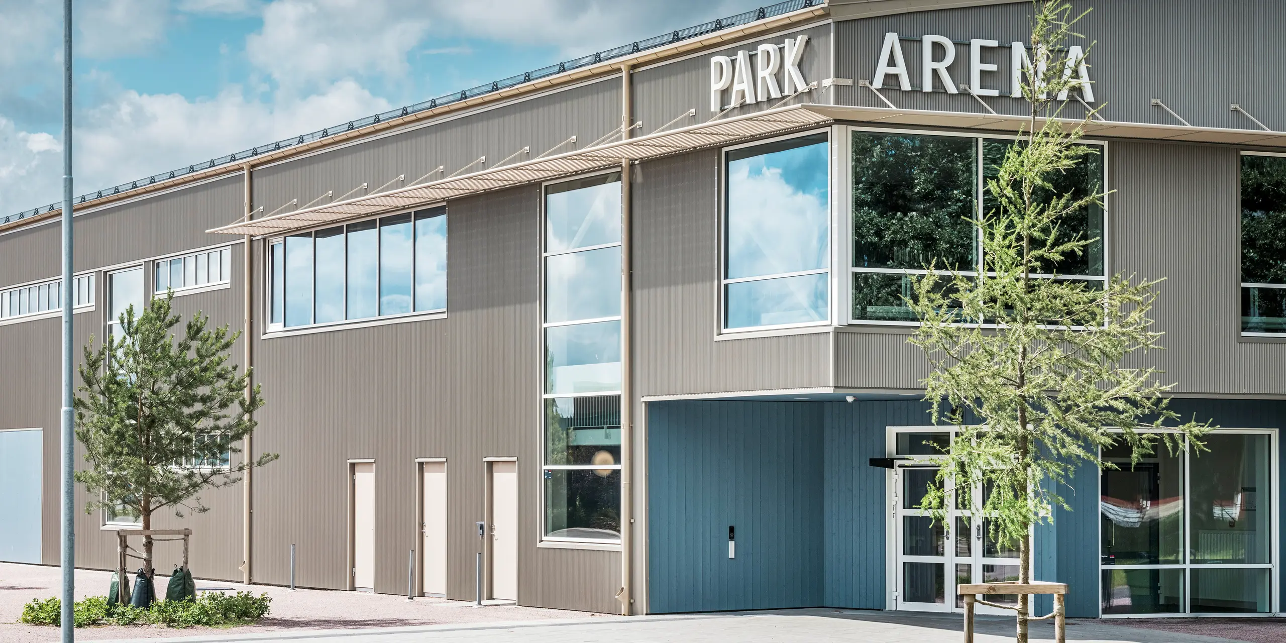 Eingangsbereich der Park Arena in Värnamo, Schweden, mit moderner Fassadengestaltung in Form des stranggepressten PREFA Zackenprofils in Bronze. Die langlebige und witterungsbeständige Aluminium-Fassade verleiht der 3.300 m² großen Sporthalle ein elegantes und markantes Erscheinungsbild. Das PREFA Zackenprofil sorgt für faszinierende Licht- und Schatteneffekte, die das architektonische Design der Arena hervorheben.