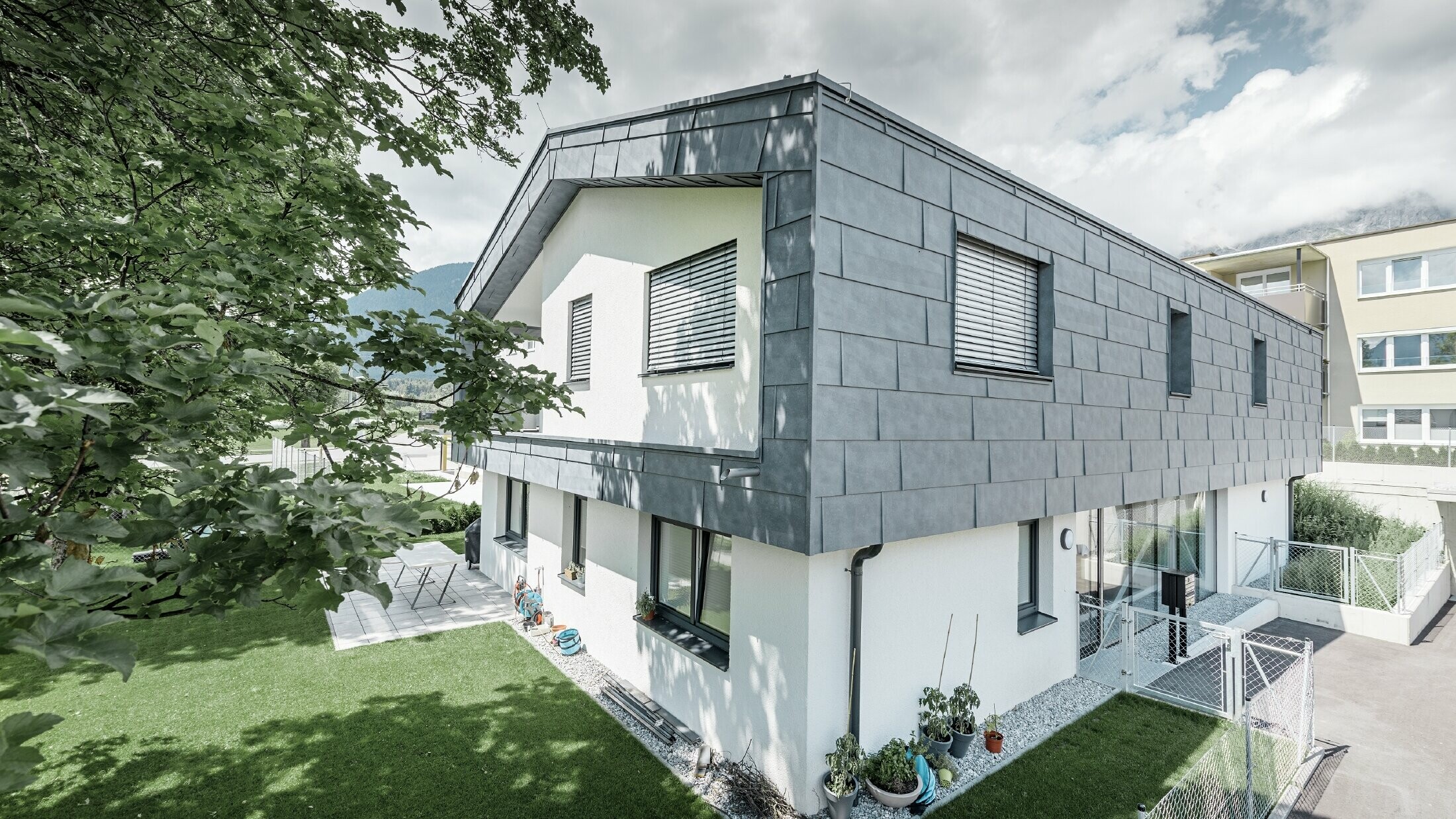Moderne tilbygg på et bolighus med flatt saltak og uten takfremspring.  Fasadekledningen er utført med PREFA fasadepanel FX.12 i steingrå.