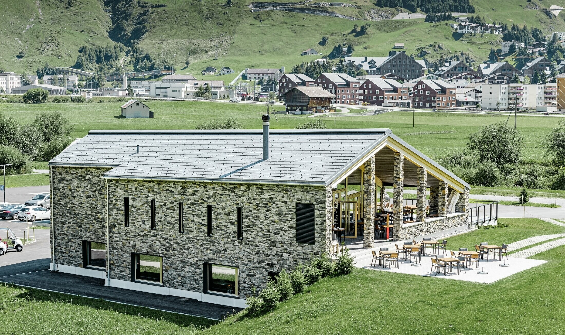 Moderne klubbhus på golfbanen i Andermatt med steinfasade og PREFA FX.12 aluminiumstakpanel i steingrå