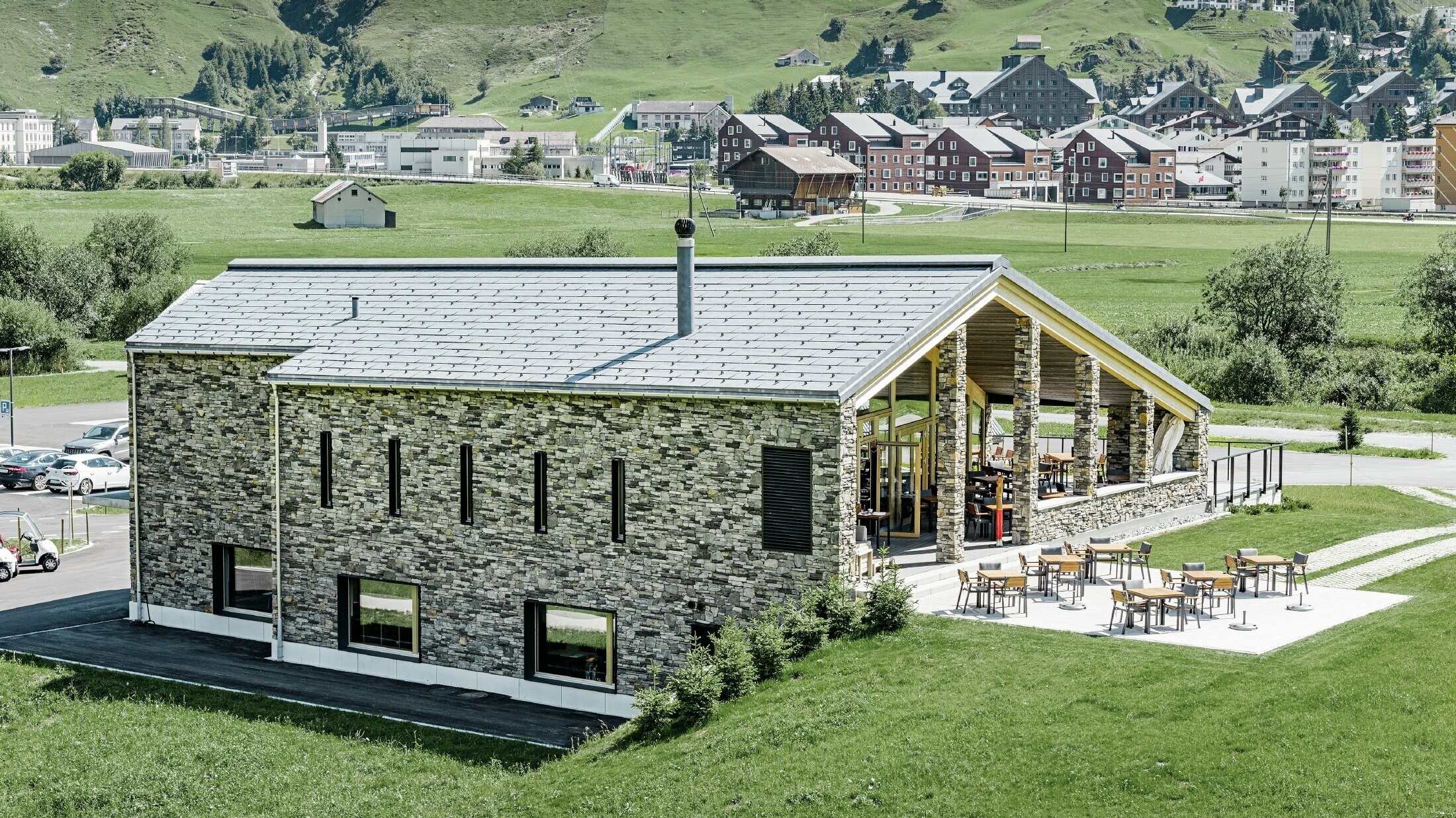 Moderne klubbhus på golfbanen i Andermatt med steinfasade og PREFA FX.12 aluminiumstakpanel i steingrå