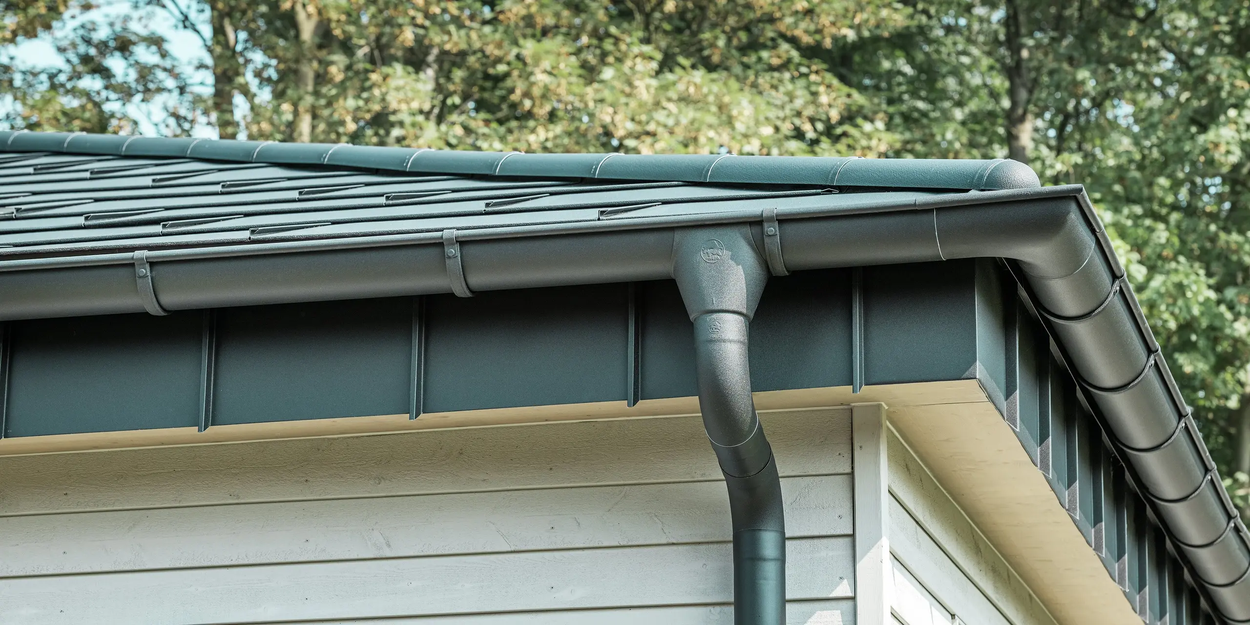 Detaljbilde av PREFA takdrenering på en bungalow i Rommerskirchen. Den høykvalitets fotrenna og nedløpsrøret i P.10 svart gir sikker takdrenering ved regn. De holdbare PREFA aluminiumsproduktene kombinerer funksjonalitet med moderne, elegant design.