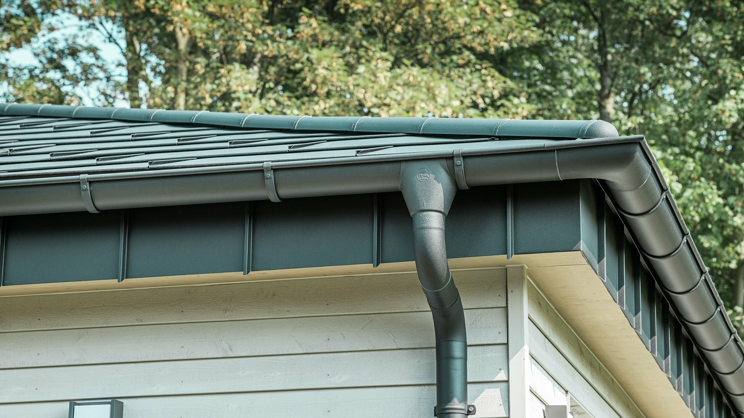 Detaljbilde av PREFA takdrenering på en bungalow i Rommerskirchen. Den høykvalitets fotrenna og nedløpsrøret i P.10 svart gir sikker takdrenering ved regn. De holdbare PREFA aluminiumsproduktene kombinerer funksjonalitet med moderne, elegant design.