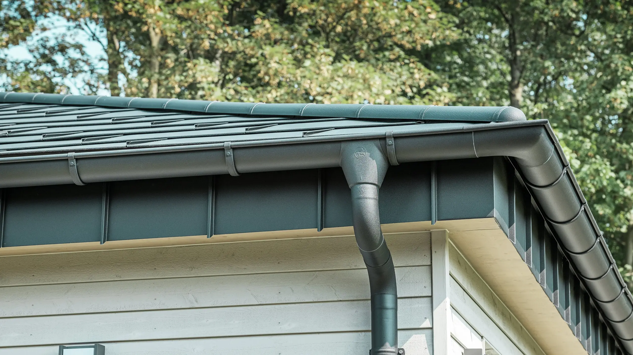 Detaljbilde av PREFA takdrenering på en bungalow i Rommerskirchen. Den høykvalitets fotrenna og nedløpsrøret i P.10 svart gir sikker takdrenering ved regn. De holdbare PREFA aluminiumsproduktene kombinerer funksjonalitet med moderne, elegant design.