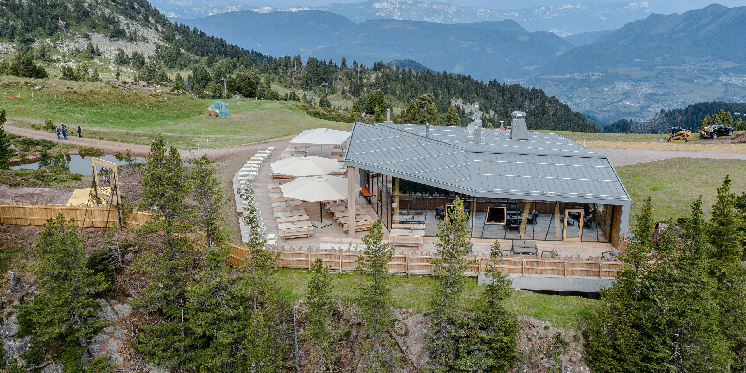 Eindrucksvoller Blick auf das Ristorante Busabelle, eingebettet in die alpine Landschaft mit einem Panoramablick auf weitläufige Täler und entfernte Bergketten. Das Restaurant zeichnet sich durch seine moderne Konstruktion mit einer hellgrauen PREFALZ Dach- und Fassadenverkleidung sowie natürlichen Holzelementen aus. Die großzügige Terrasse ist mit Sonnenschirmen und Holztischen ausgestattet, die den Gästen ein entspannendes Ambiente für Mahlzeiten in der freien Natur bieten. Die widerstandsfähige Aluminiumhülle bietet den Gästen Schutz vor alpinen Witterungen. 