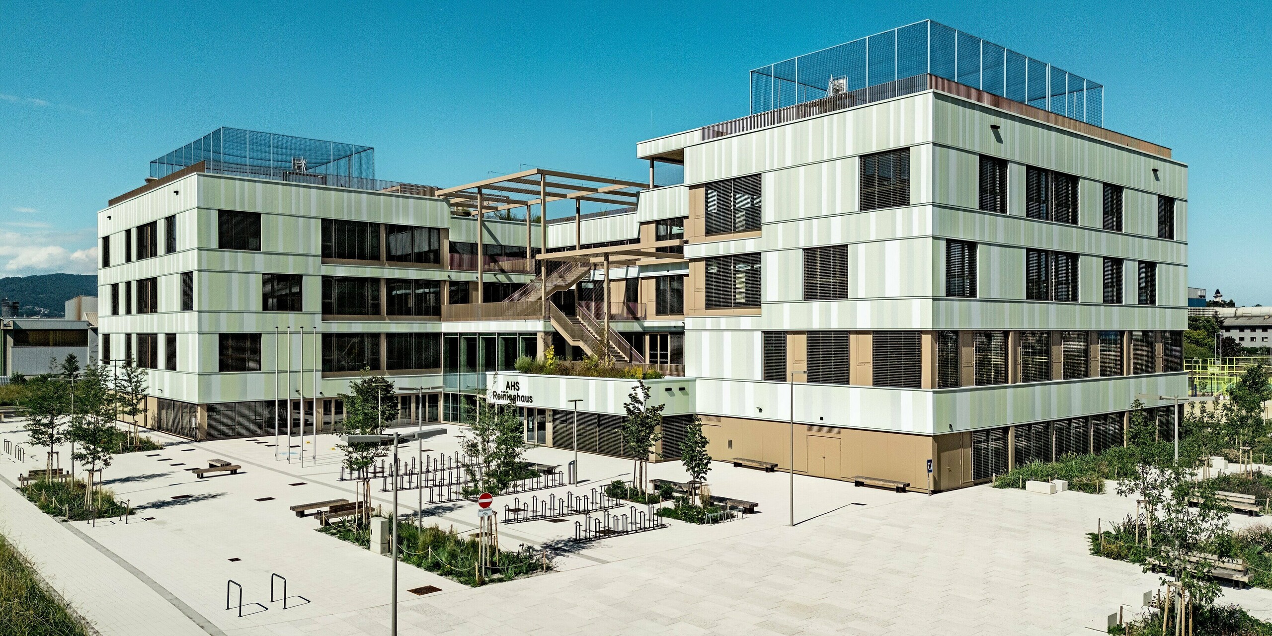 Die AHS Reininghaus in Graz begeistert mit ihrer modernen Architektur, die durch die PREFA Sidings in Sonderfarben hervorgehoben wird. Die Fassadenverkleidung aus Aluminium in sanften Grün- und Weißtönen sorgt für ein frisches, elegantes Erscheinungsbild. Besonders auffällig ist die gelungene Kombination aus der strukturierten Fassade und den Fensterläden, die das Gebäude sowohl optisch aufwerten als auch für Privatsphäre und Sonnenschutz sorgen. Diese Kombination aus ästhetischem Design und langlebiger Materialqualität garantiert eine funktionale, pflegeleichte und energieeffiziente Lösung, die im städtischen Umfeld von Graz herausragt.