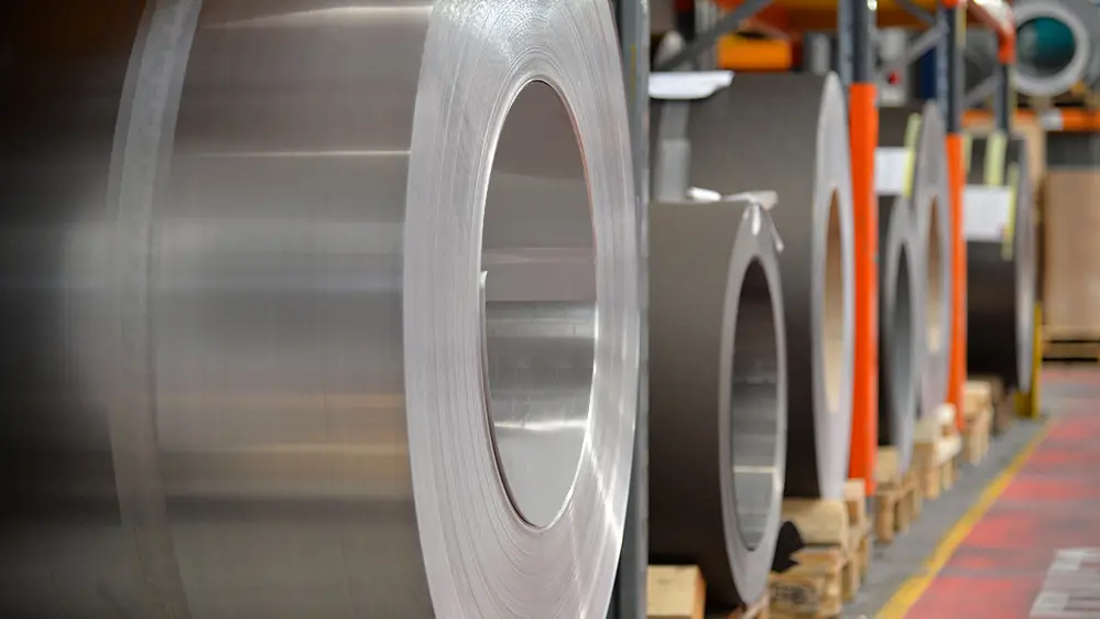 Aluminiumsruller (coils) lagret på trepaller, i forgrunnen er en naturlig blank aluminiumsspole, bak den ses andre bånd og plater av aluminium.