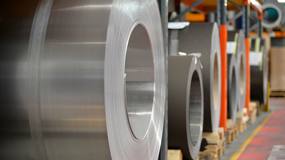 Aluminiumsruller (coils) lagret på trepaller, i forgrunnen er en naturlig blank aluminiumsspole, bak den ses andre bånd og plater av aluminium.