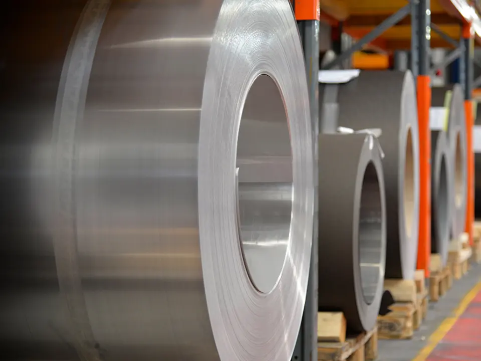 Aluminiumsruller (coils) lagret på trepaller, i forgrunnen er en naturlig blank aluminiumsspole, bak den ses andre bånd og plater av aluminium.