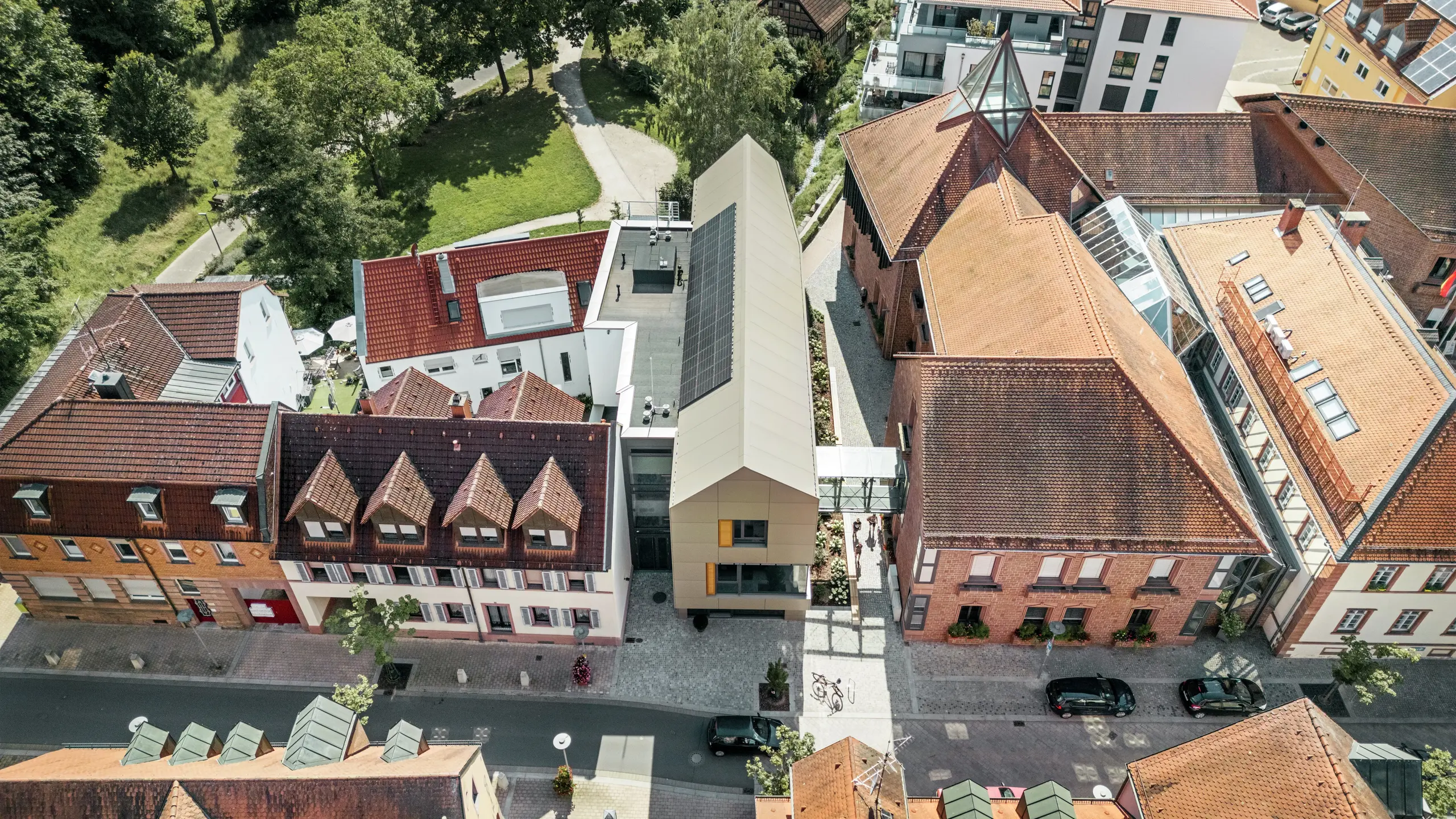Das Rathaus in Alzenau liegt im Herzen eines historischen Stadtviertels, umgeben von traditionellen Gebäuden mit roten Ziegeldächern. Im Kontrast dazu steht das moderne Rathaus mit seiner eleganten, bronzefarbenen Fassade aus PREFA-Aluminium-Verbundplatten. Die innovative Architektur hebt sich deutlich von den benachbarten klassischen Gebäuden ab und fügt sich gleichzeitig harmonisch in das Stadtbild ein.
