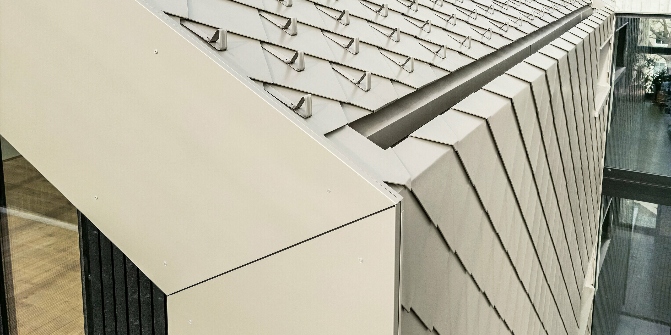 Nahaufnahme des Dachs eines architektonisch beeindruckenden Mehrfamilienhauses in Dresden, Deutschland, verkleidet mit der PREFA Aluminiumraute 29 × 29 in Bronze. Das Bild zeigt die präzise verarbeiteten Rauten auf dem Dach und die Übergänge zur Fassade. An der Traufe wurden die Rauten leicht geknickt, um einen homogenen Gesamteindruck zu gewährliesten. Das robuste und hochwertige Blech sorgt für Langlebigkeit und verleiht dem Gebäude zugleich eine elegante, moderne Optik.