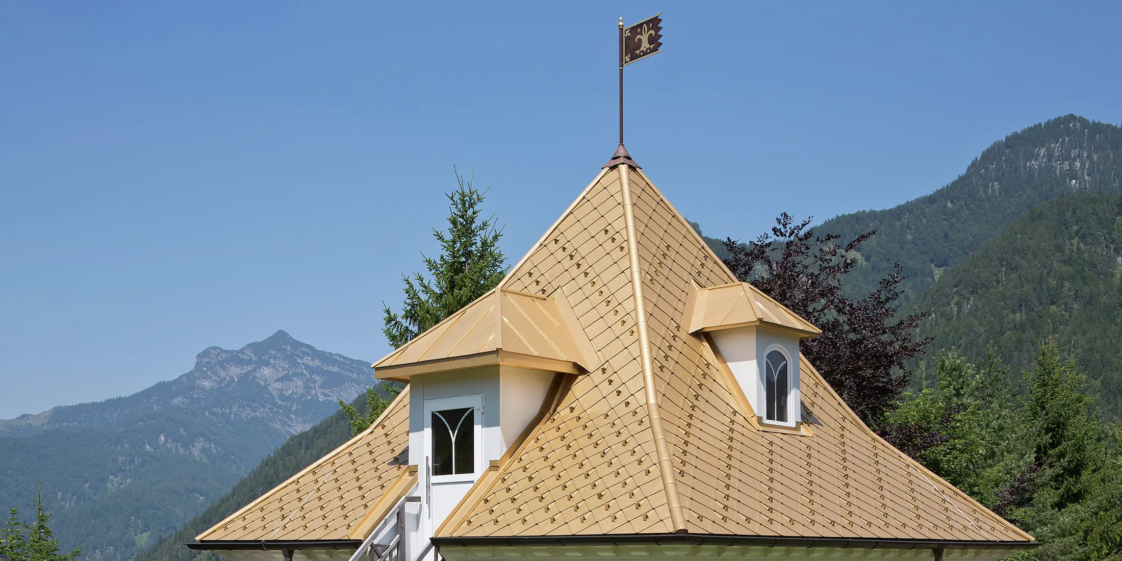 Detailansicht des Aluminiumdaches eines kleinen Anbaus. Das Goldene Dach liegt in Tirol, umgeben von einem gepflegten Garten und einer beeindruckenden Alpenkulisse.