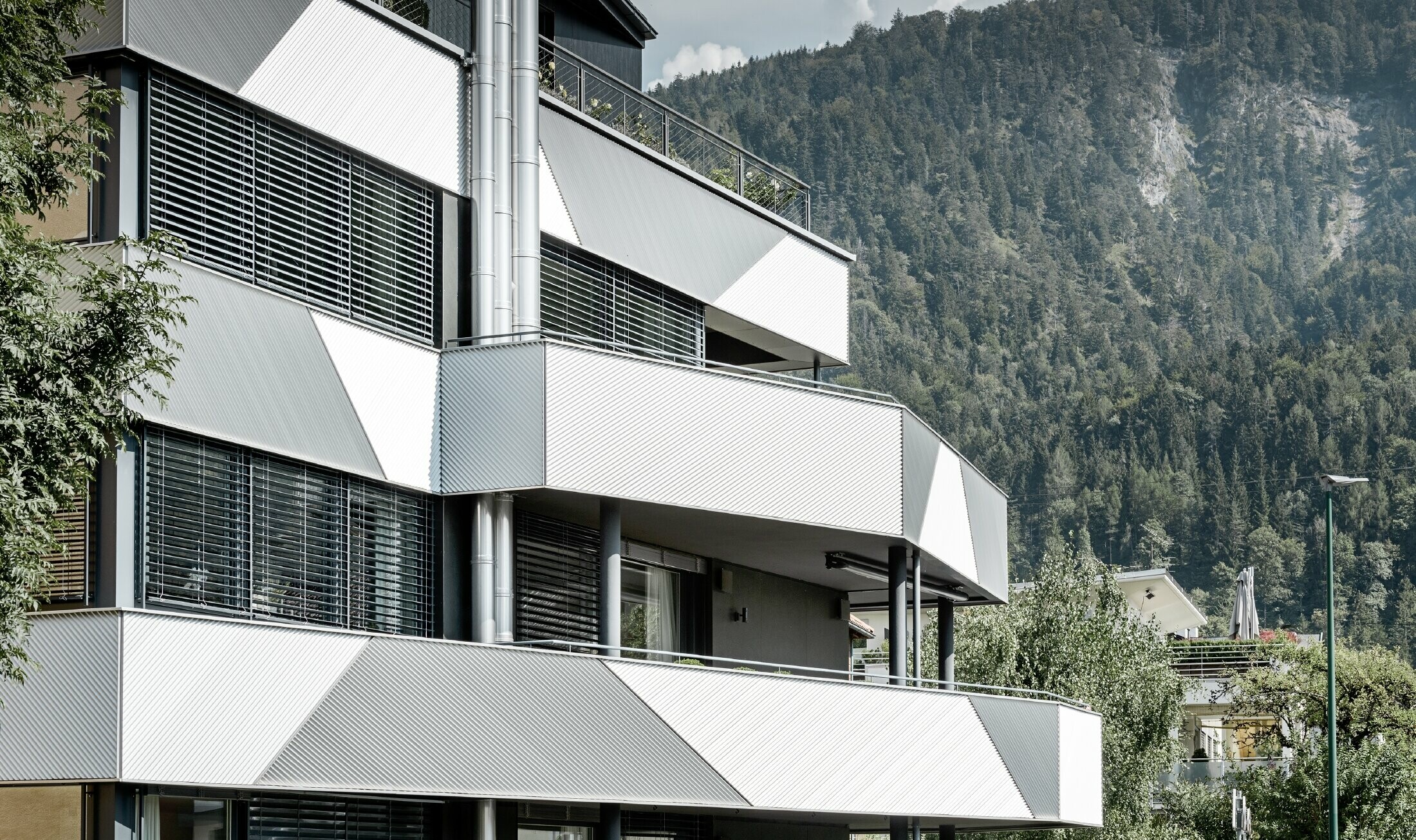 Fasadeutforming for et appartementshus med balkonger og overbygde ganger med skråmontert PREFA sikksakkprofil.