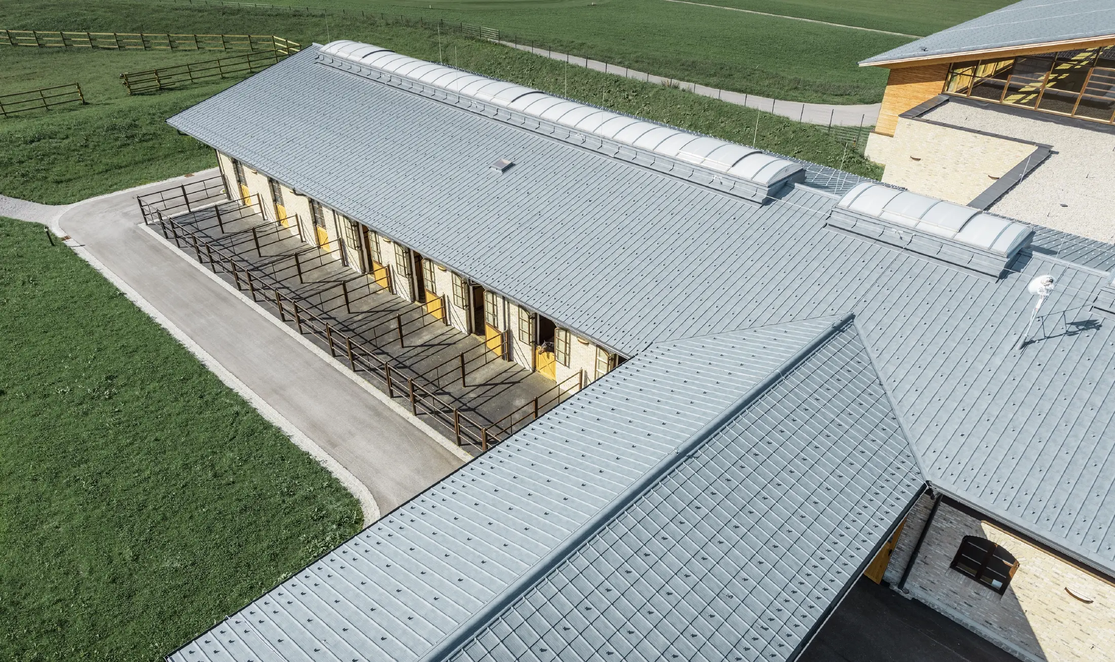 Foto av av stutteriet i Thalgau i fugleperspektiv. Ridehallen er kledd med PREFA takplate i steingrå.