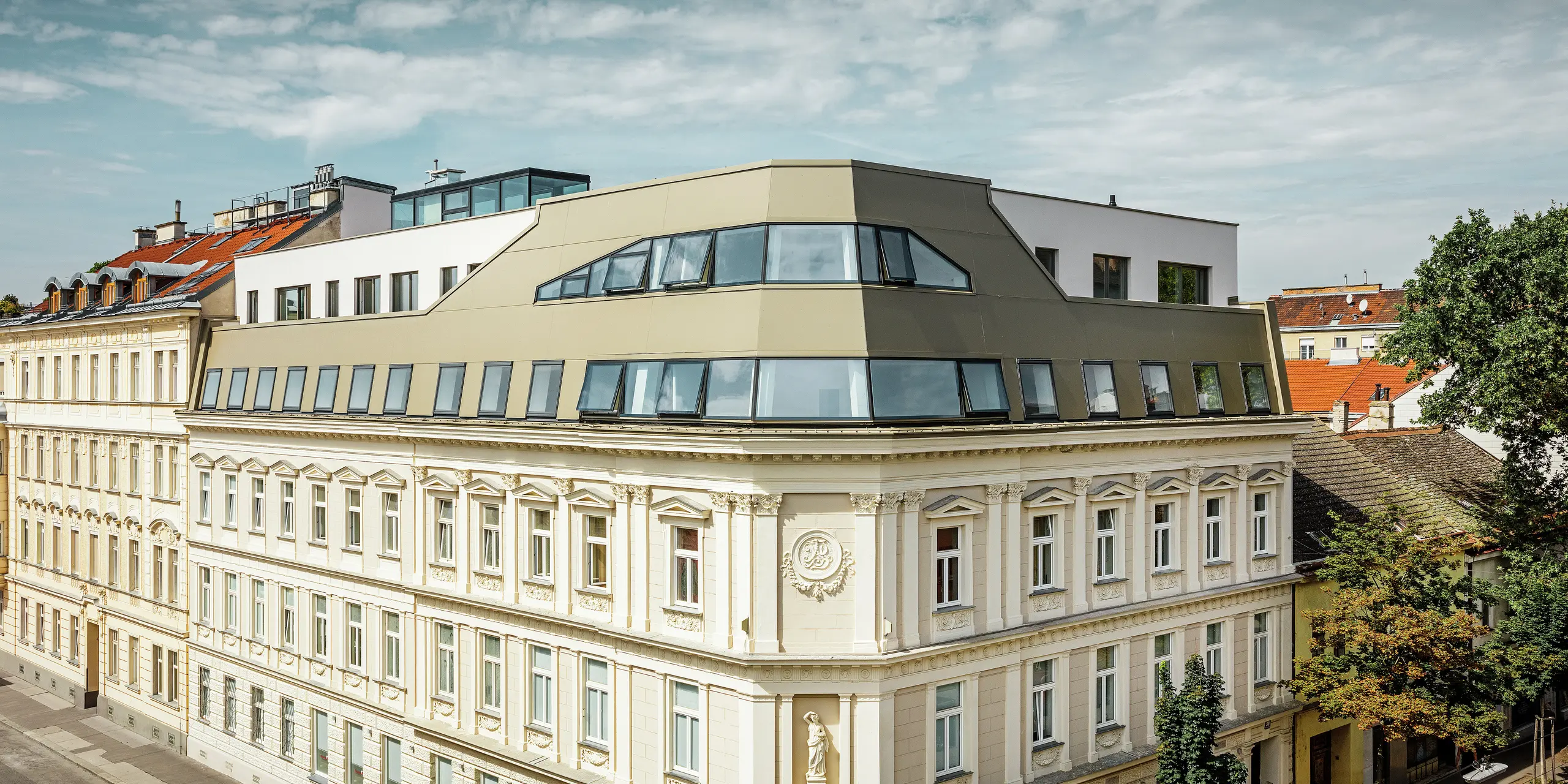 Gesamtansicht des Dachflächenausbaus in der Schloßhofer Straße in Wien mit der Aluminium Verbundplatte in Bronze. Der komplette Dachausbau des historischen Gebäudes in Wien überzeugt durch die harmonische Kombination von Glas und PREFA Aluminium Verbundplatten in Bronze. Selbstbewusst, aber stilvoll schmiegt sich die neue Architektur an den klassizistischen Bestand.